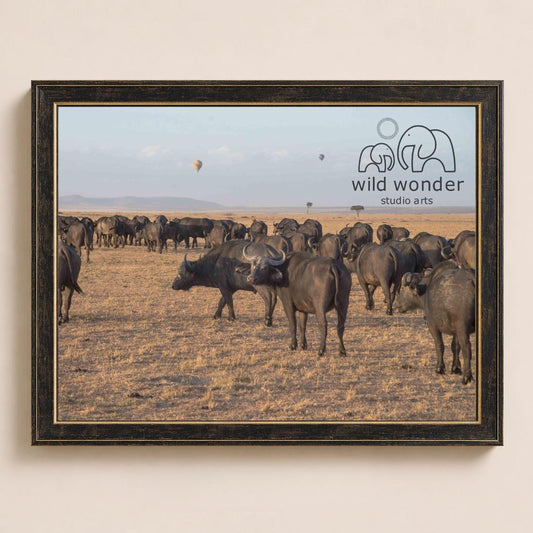 A herd of wild animals, including elephants and buffalo, grazing in a dry grassland landscape with a few hot air balloons visible in the sky.