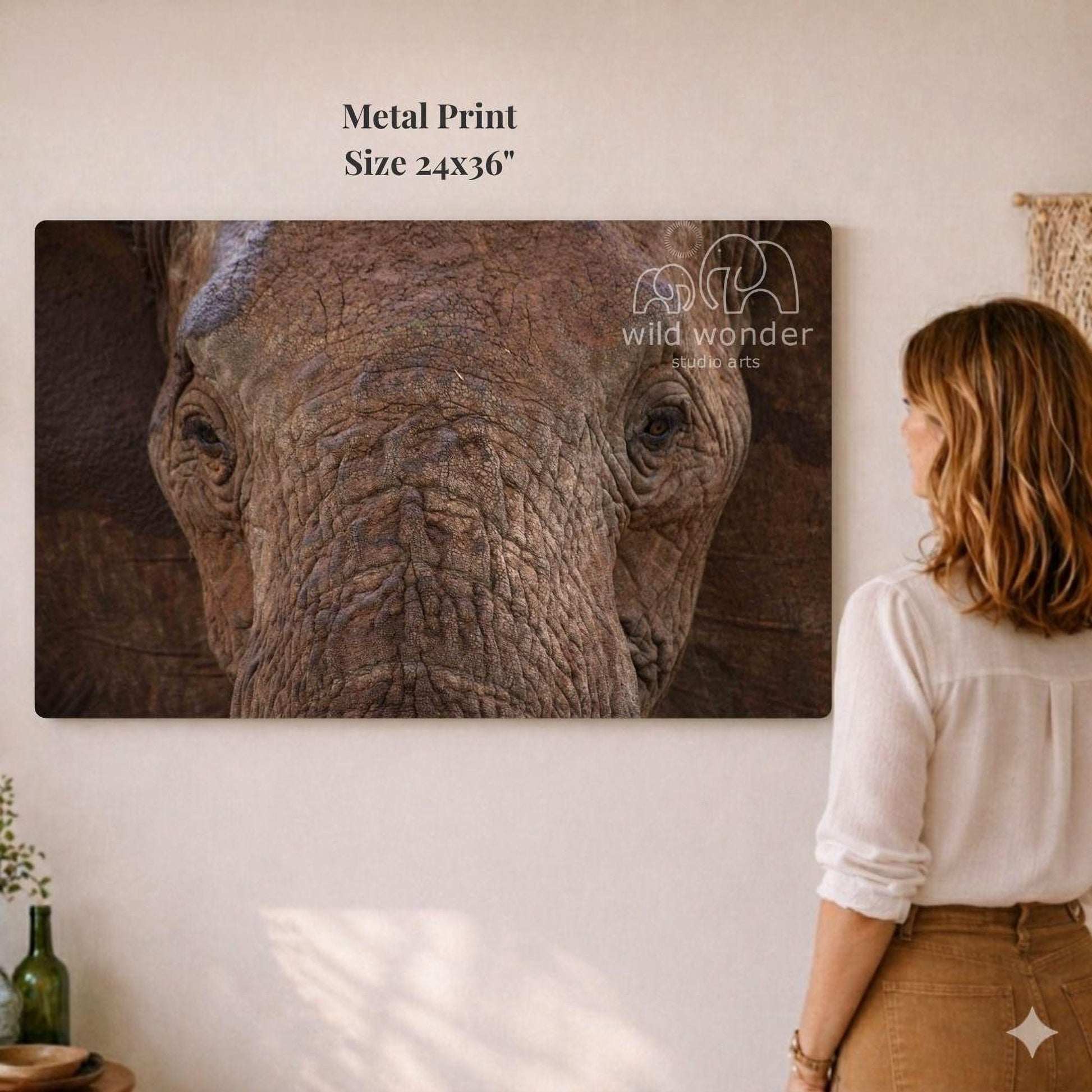 A woman is standing in front of a large metal print of an elephant's face, looking at it with interest.