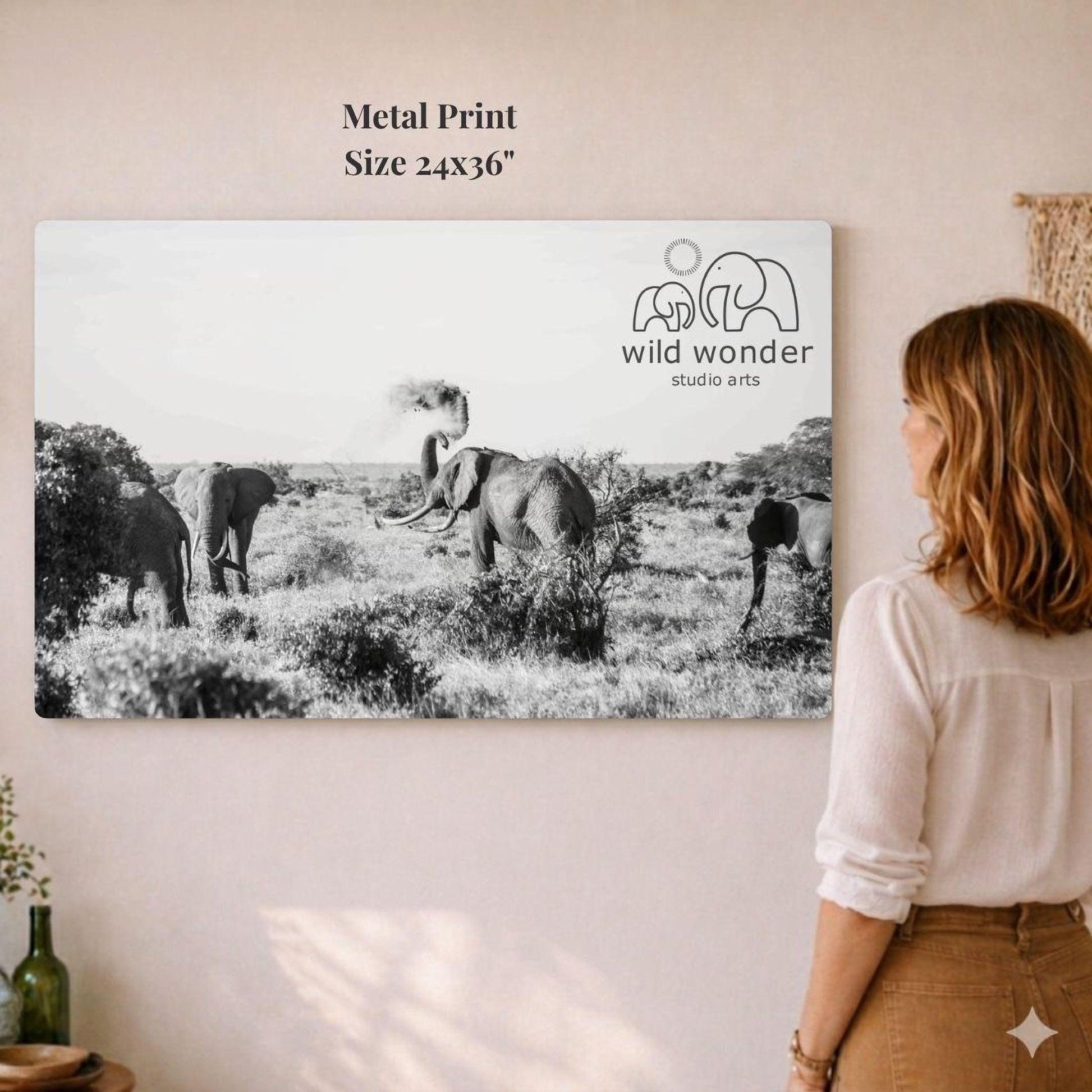 A woman is standing in front of a large metal print depicting a group of elephants in a field.
