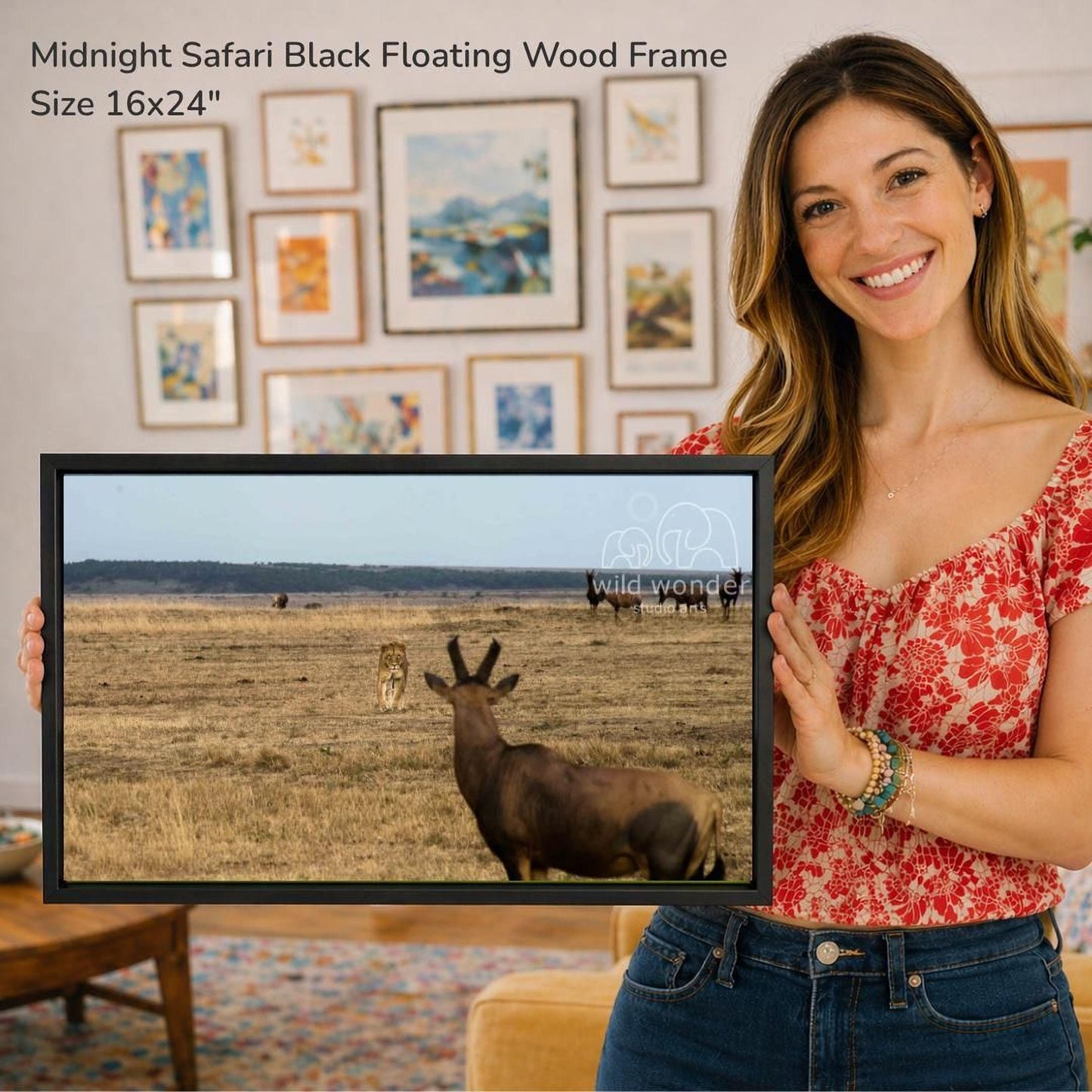 A woman is holding up a framed photograph of a wild animal, likely a lion, in a grassy field. The photograph is of a safari scene, and the woman is smiling and posing with the framed image.