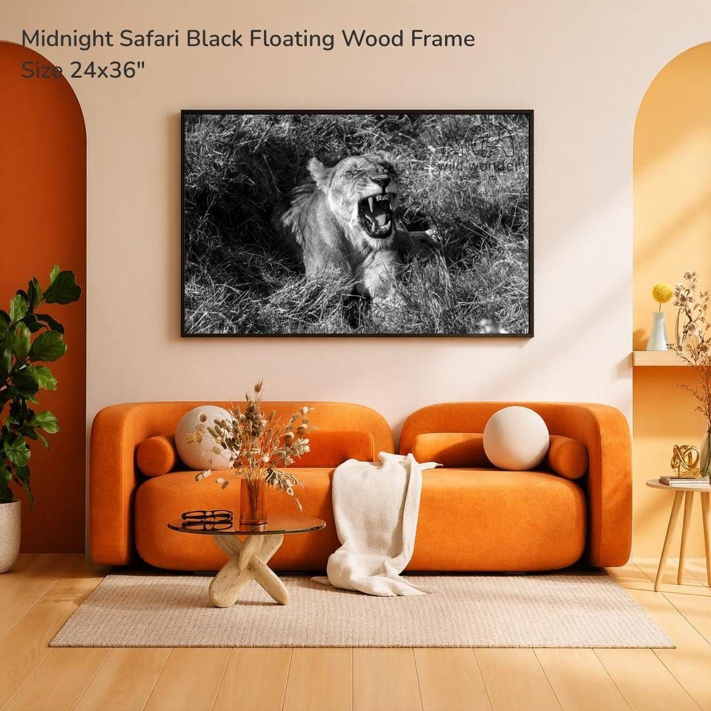 a large black and white photograph of a lion on a grassy field, hanging on a wall above an orange sofa in a living room setting.