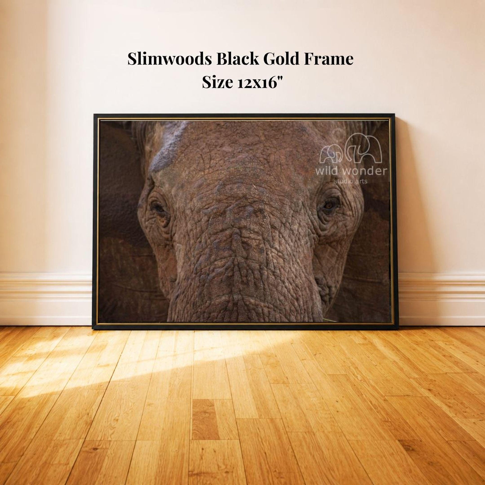 A close-up photograph of an elephant's face is displayed on a black frame, mounted on a wooden floor against a white wall.