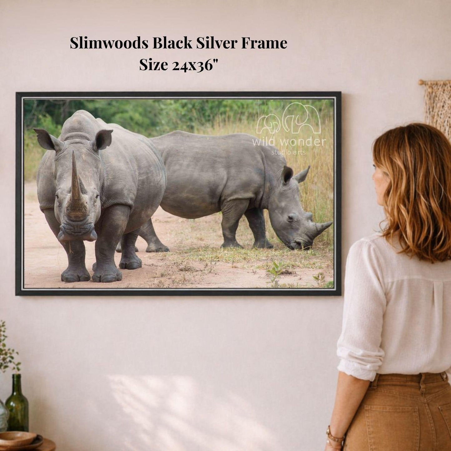 A woman is standing in front of a framed photograph of two rhinos, one standing and one walking, on a wall.
