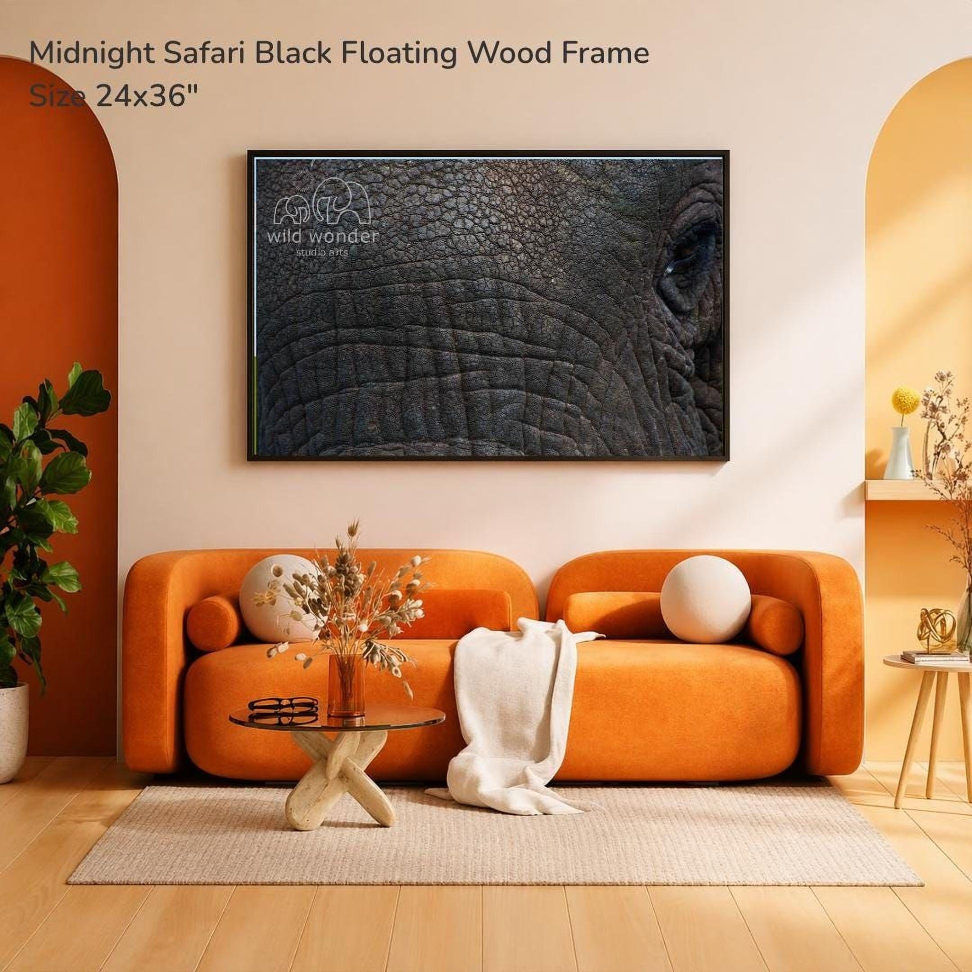 a large, black, and textured elephant image displayed on a wall above an orange sofa with a glass coffee table in front of it.