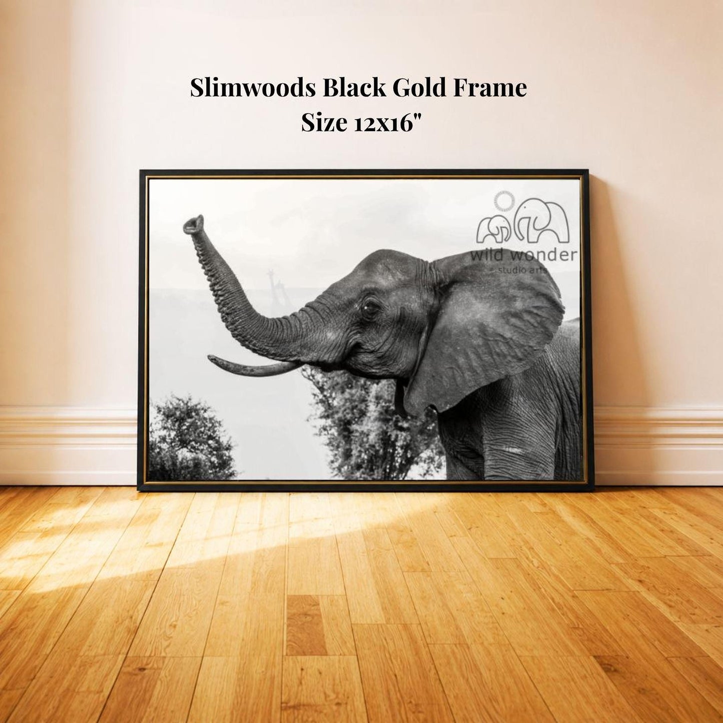 A black and white photograph of an elephant standing on a wooden floor, with a framed image of the elephant on the wall behind it.
