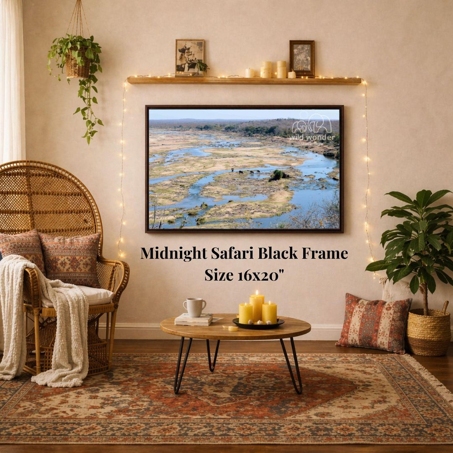 a living room with a large framed picture of a safari landscape hanging on the wall. The room has a wicker chair, a coffee table, and a potted plant. The picture is described as a "Midnight Safari Black Frame" and is 16x20 inches in size.