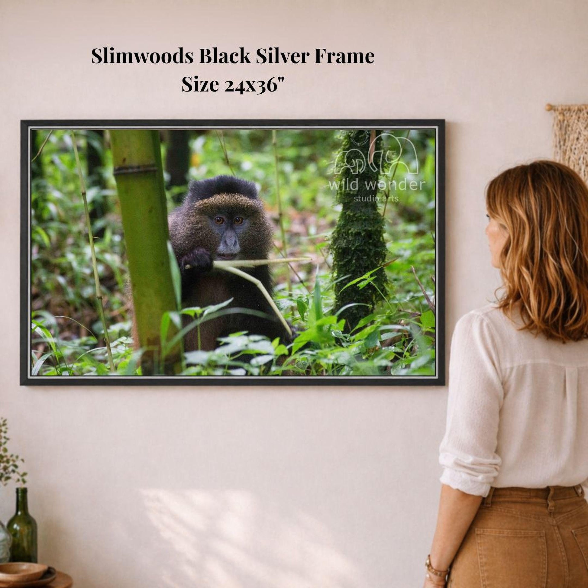A woman is standing in front of a framed photograph of a monkey in a forest, looking at the picture.