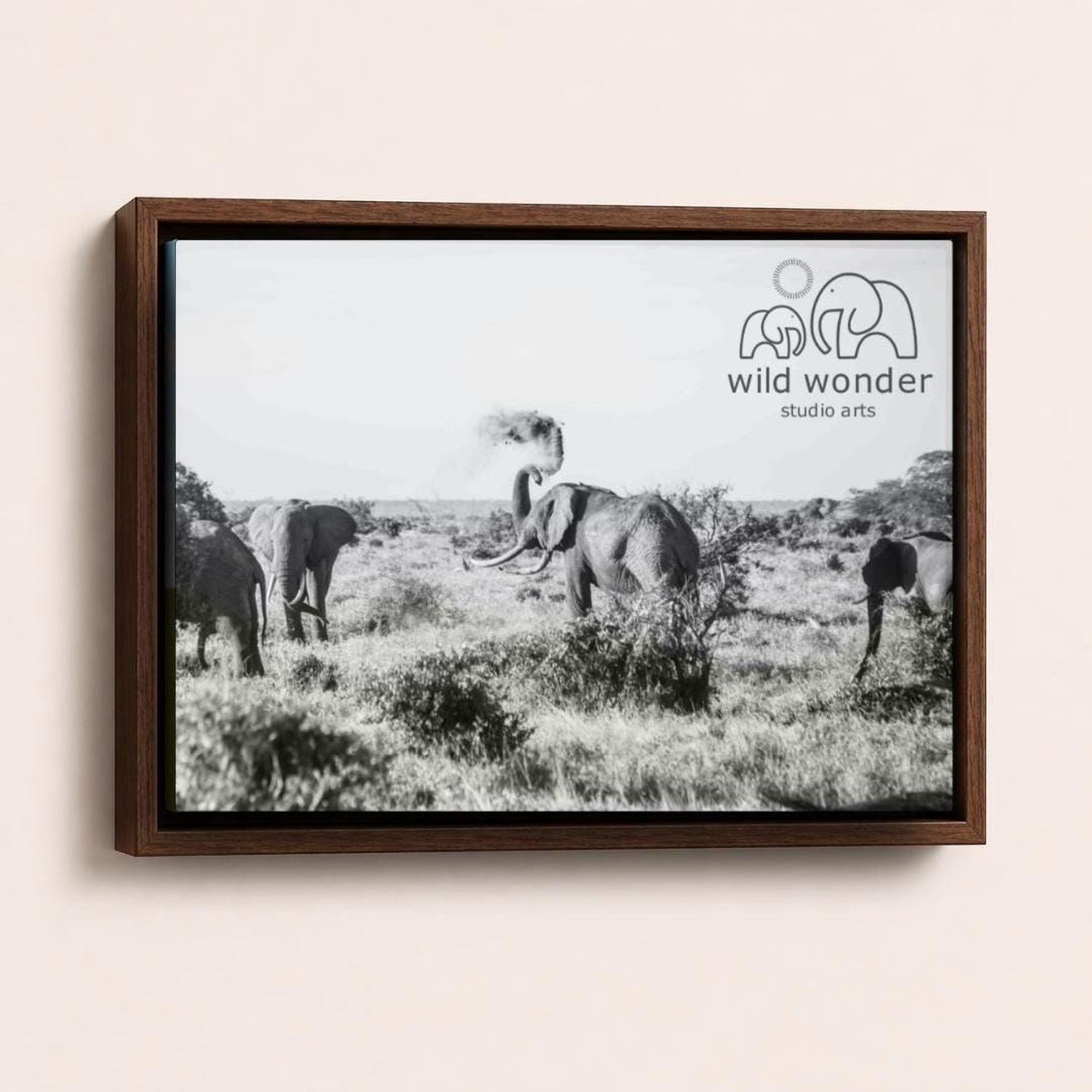 A black and white photograph of a herd of elephants in a grassy field, with the text "wild wonder studio arts" displayed in the top right corner.