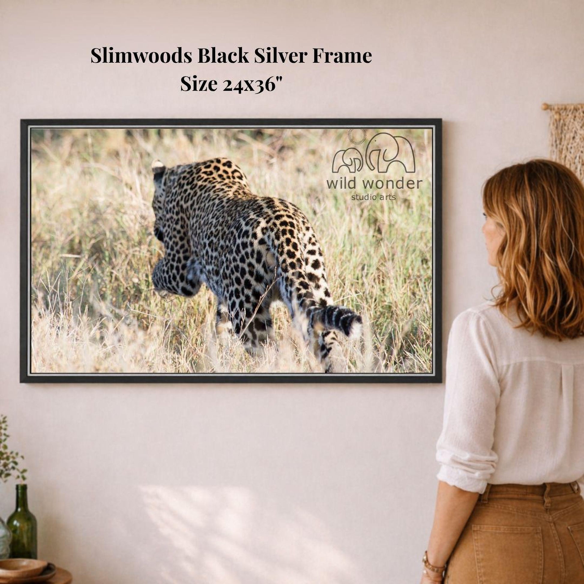 A woman is standing in front of a framed photograph of a leopard in a grassy field, observing the animal.