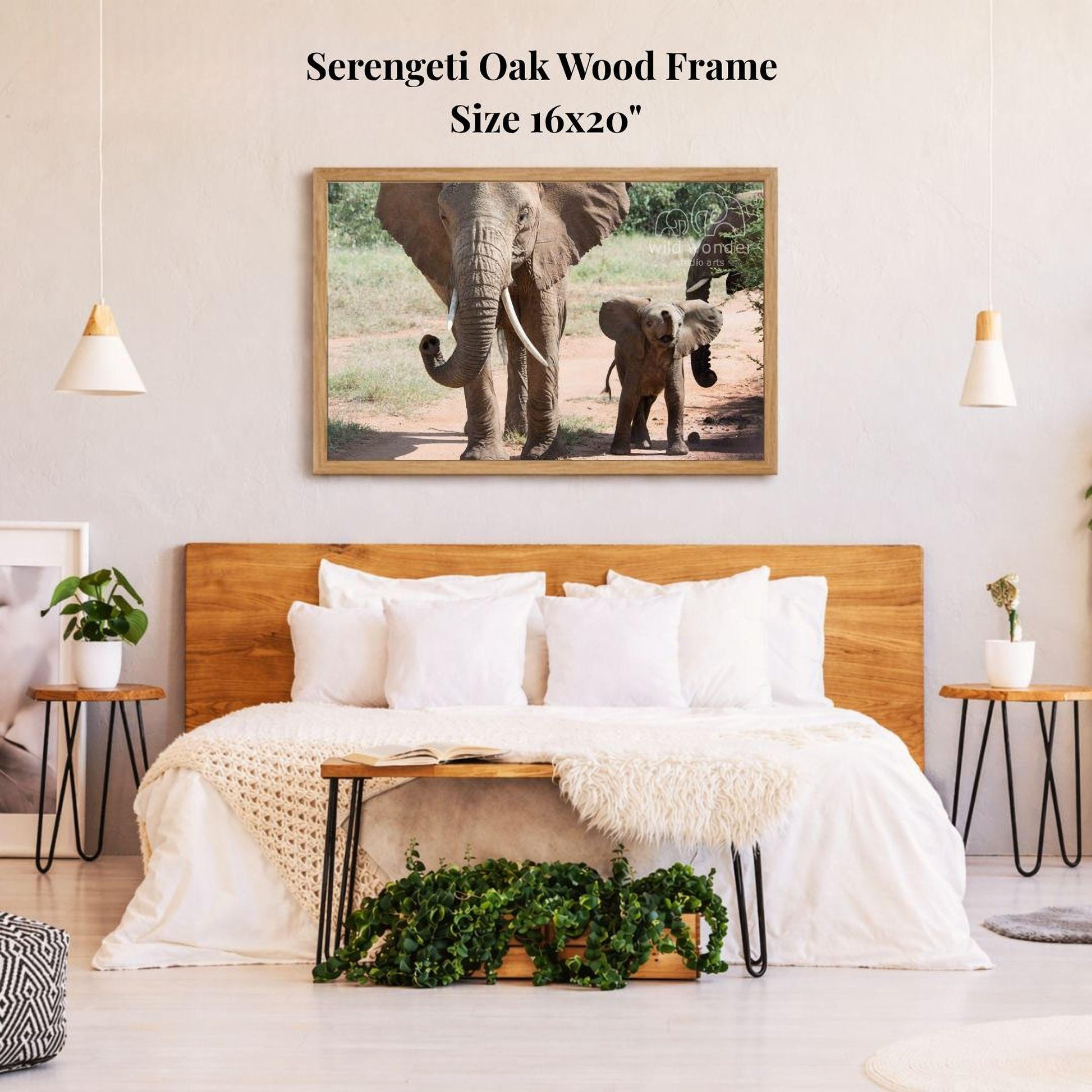a serene bedroom scene with a large wooden headboard, a cozy bed with white pillows, and a framed photograph of two elephants walking in the wild. The photograph is hanging on the wall above the bed, creating a peaceful and natural atmosphere in the room.