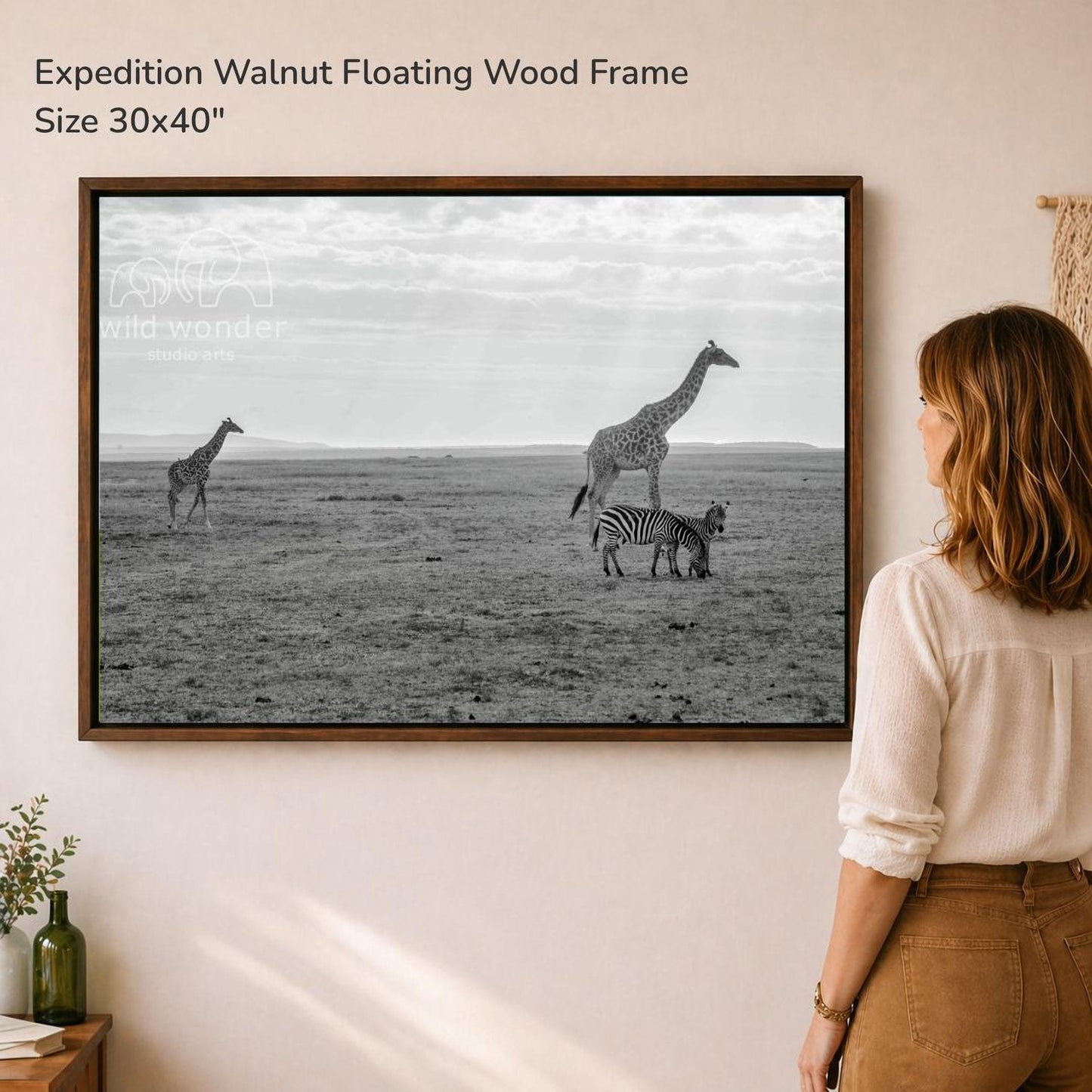 A woman is standing in front of a large framed photograph of three giraffes and a zebra in a savanna-like setting.