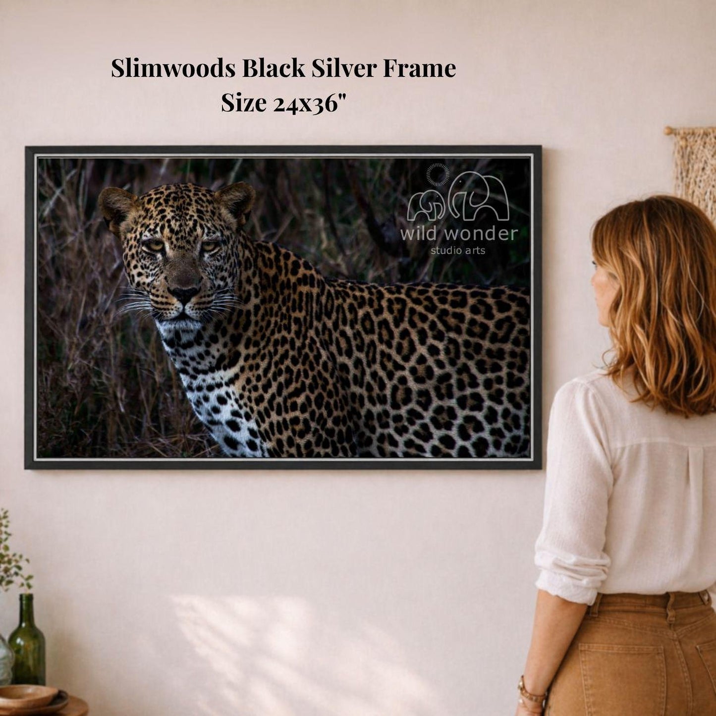 A woman is standing in front of a framed photograph of a leopard, looking at it with interest.