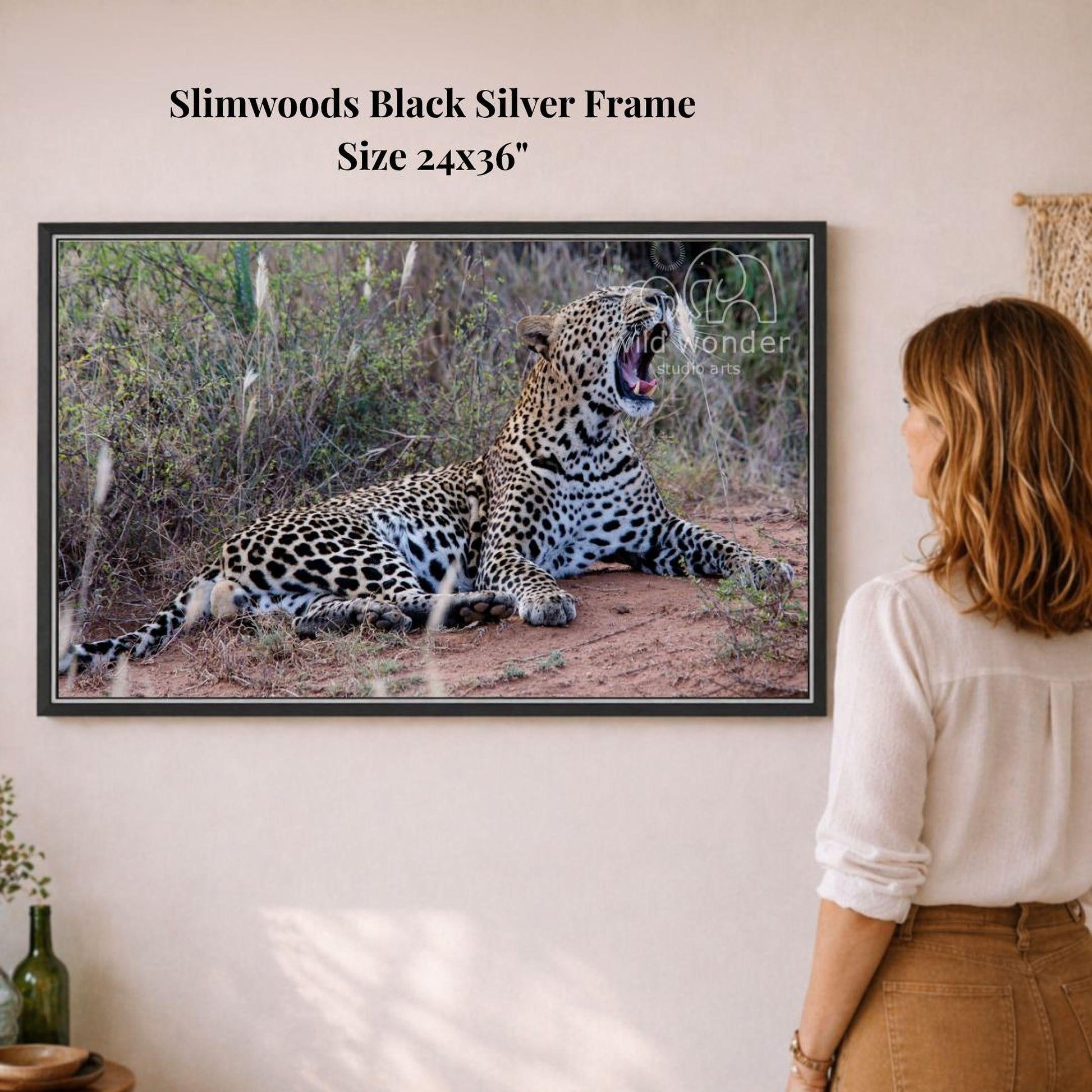 A woman is standing in front of a framed photograph of a leopard, which is lying on the ground in a natural setting.