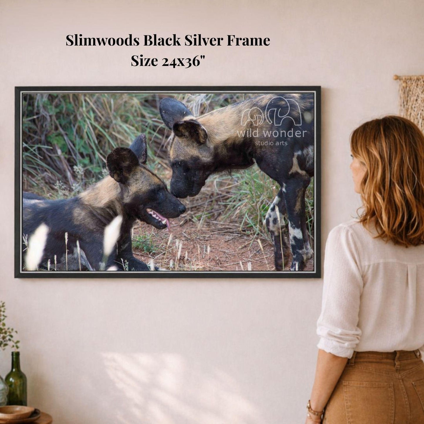 A woman is standing in front of a framed photograph of two wild dogs, one black and one brown, in a natural setting.