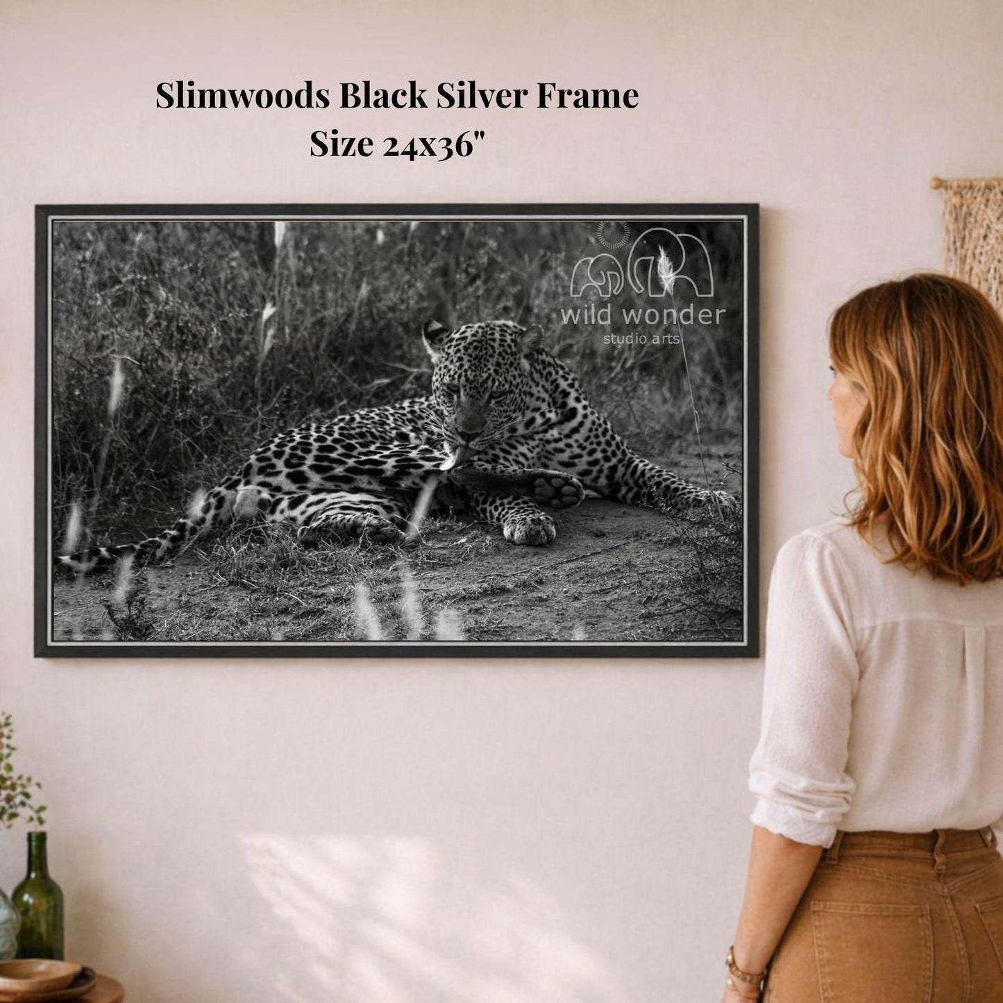 A woman is standing in front of a framed black and white photograph of a leopard resting on the ground.