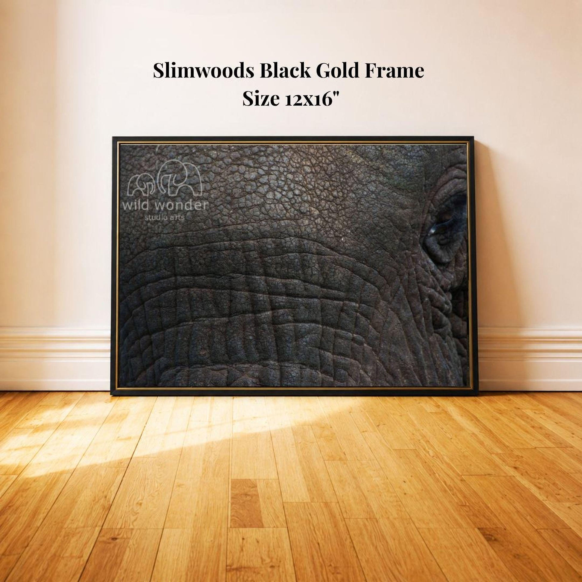 A framed photograph of an elephant's face is displayed on a wooden floor against a white wall.