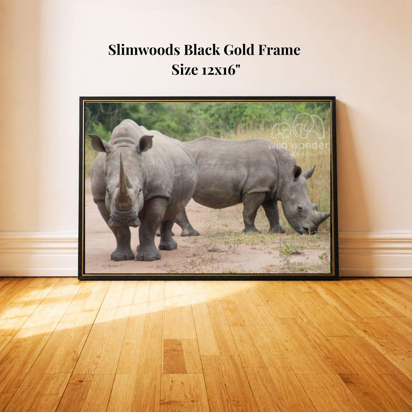 A framed photograph of two rhinoceroses standing in a grassy area, with a black gold frame.