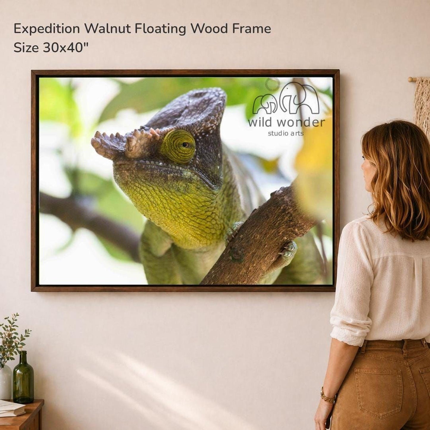 A woman is standing in front of a large framed photograph of a chameleon, which is hanging on a wall.