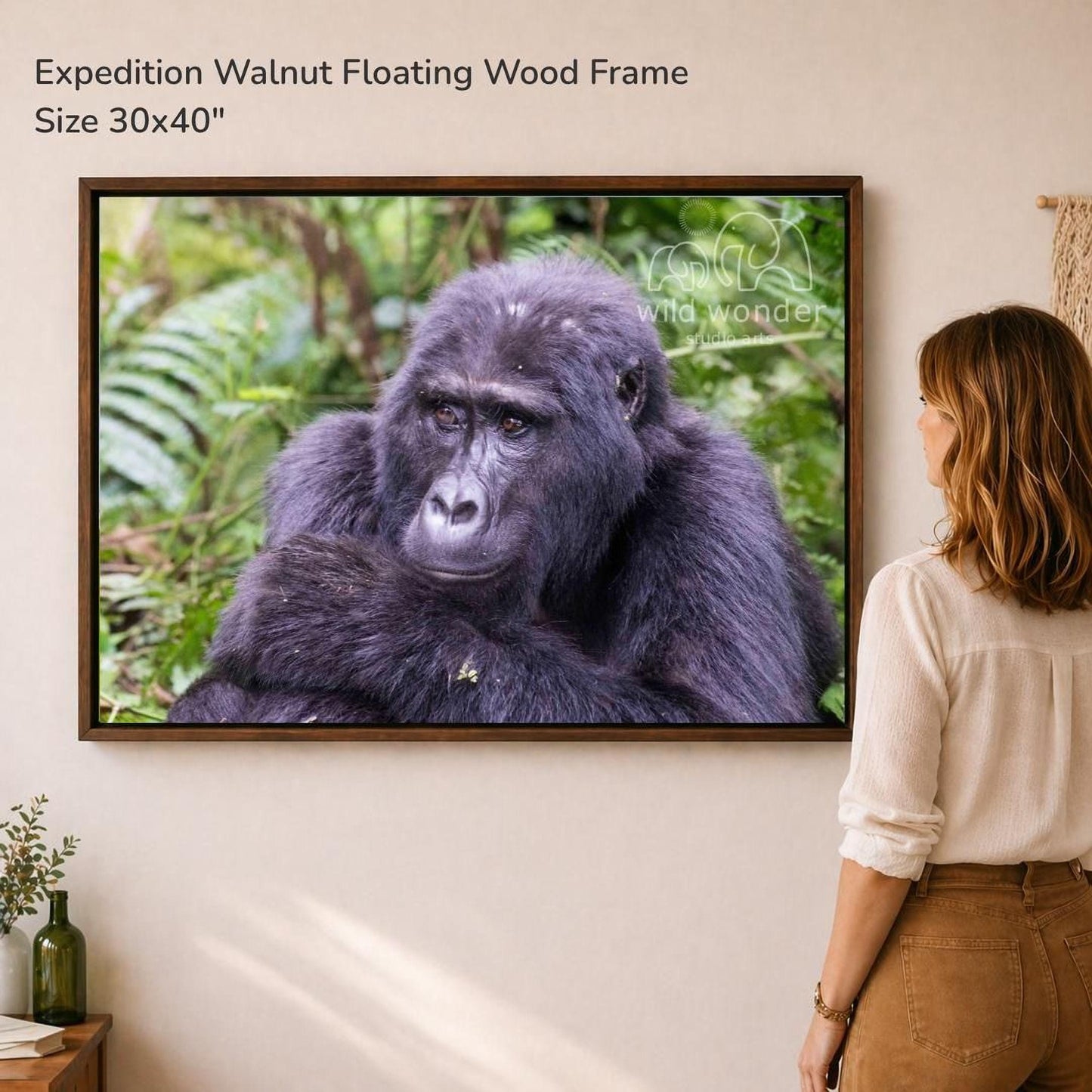 A woman is standing in front of a large framed photograph of a gorilla, which is hanging on a wall.