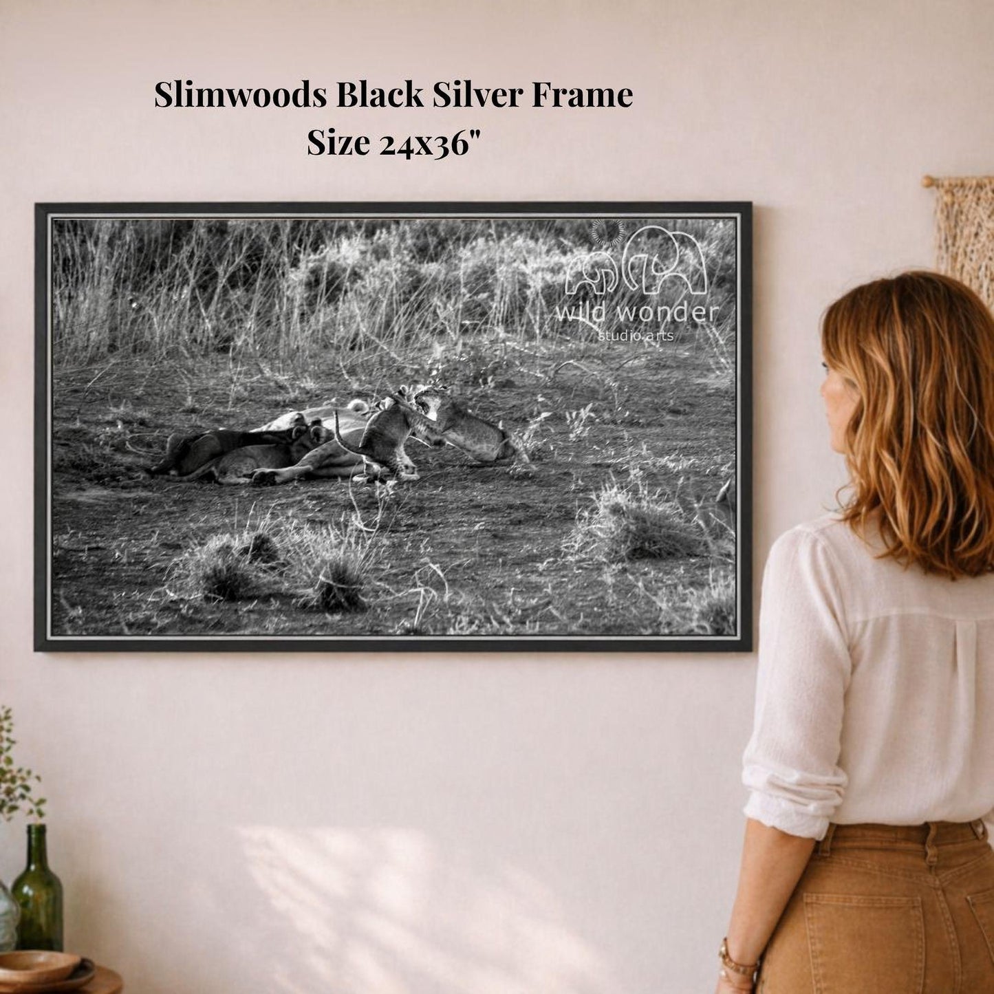 A woman is standing in front of a framed black and white photograph of a field with a dead animal lying on the ground.
