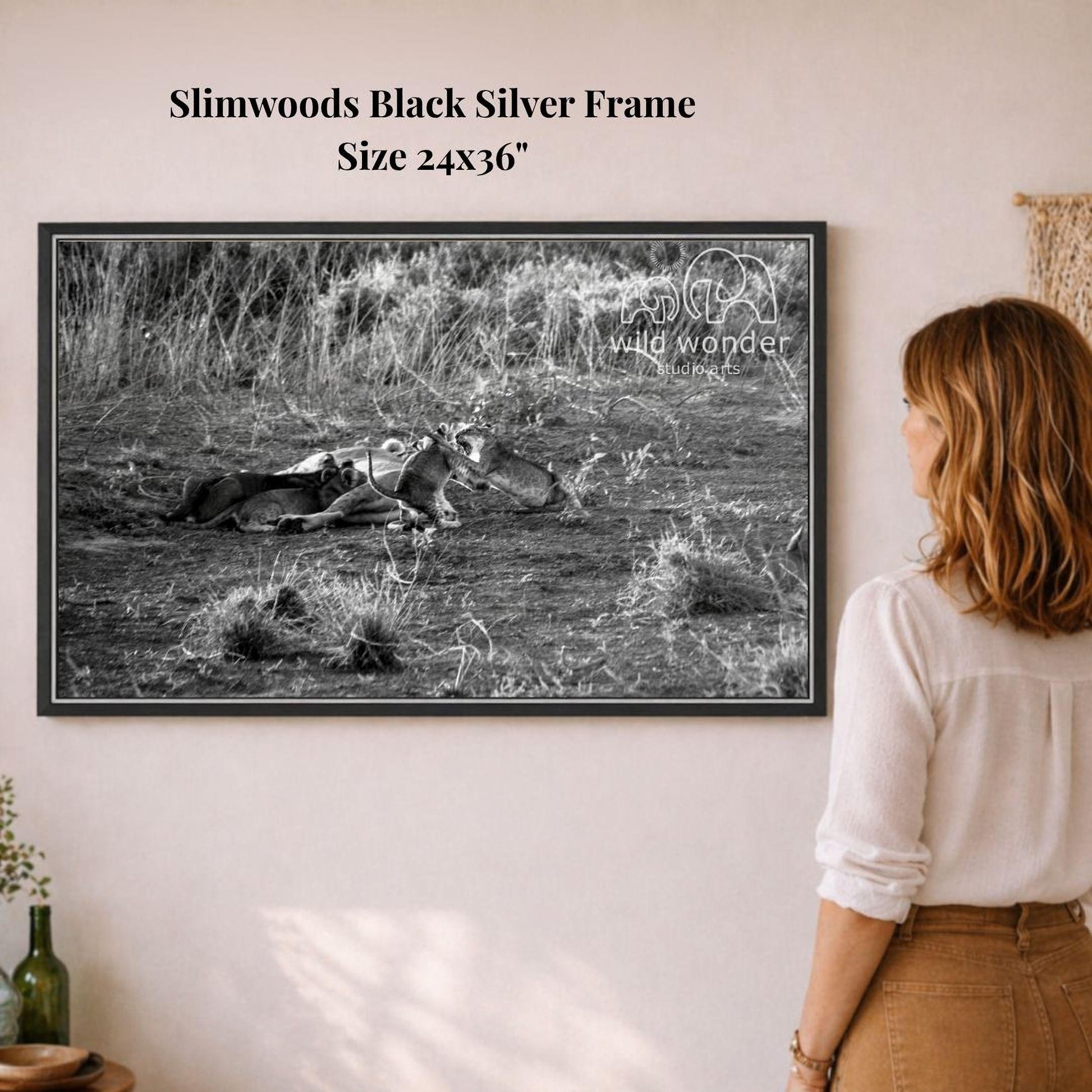 A woman is standing in front of a framed black and white photograph of a field with a dead animal lying on the ground.