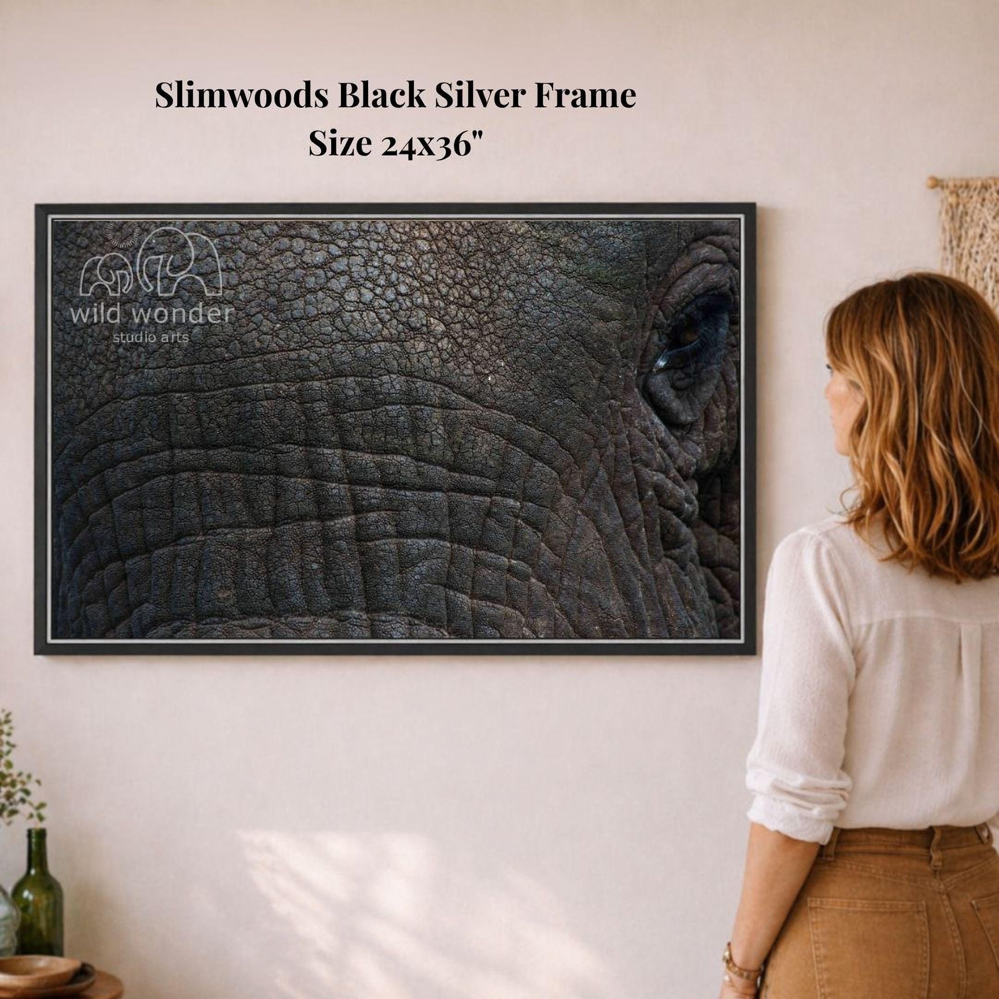 A woman is standing in front of a framed photograph of an elephant's eye, looking at it with interest.