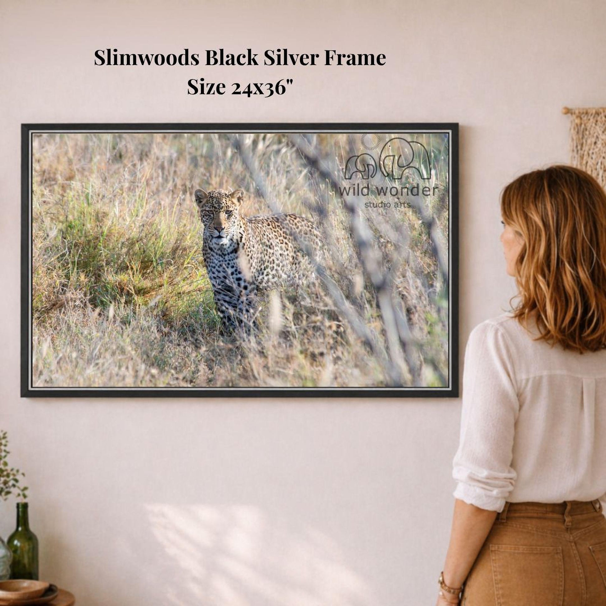 A woman is standing in front of a framed photograph of a leopard in a grassy field, observing the animal.