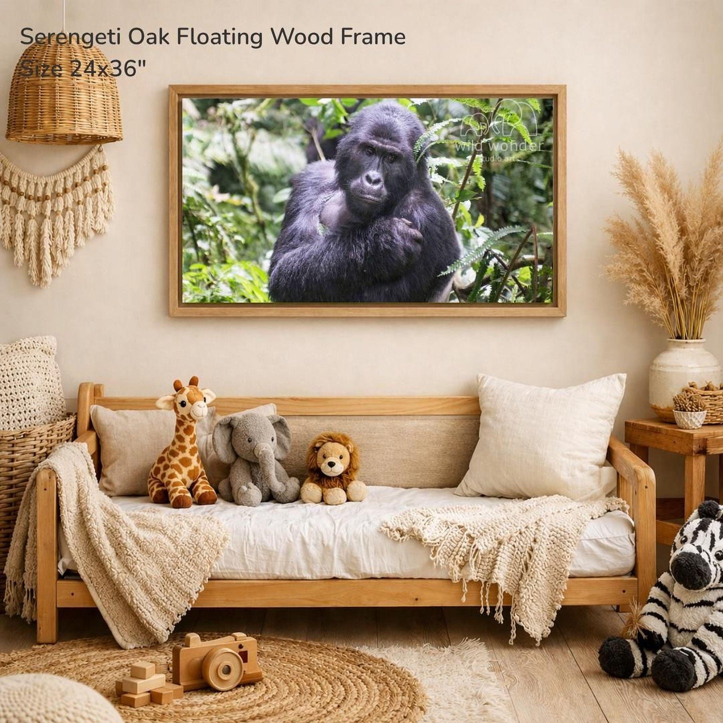 a serene indoor setting with a wooden frame hanging on a wall, displaying a photograph of a gorilla in a lush forest. The frame is described as a "Serengeti Oak Floating Wood Frame" and measures 24x36 inches. The room is decorated with various items, including a couch with stuffed animals, a wooden toy, and a woven basket.