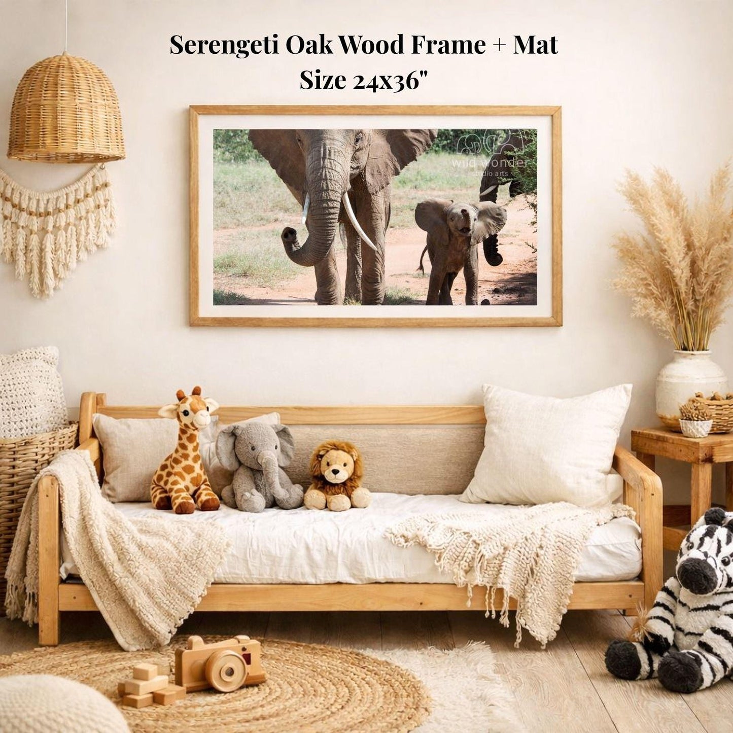 a serene indoor setting with a wooden frame and mat hanging on the wall, displaying a photograph of elephants. The room is decorated with various stuffed animals, including a giraffe, elephant, lion, and zebra, arranged on a couch and a rug. The overall atmosphere appears to be calm and inviting, with a focus on the natural beauty of the elephants in the frame.
