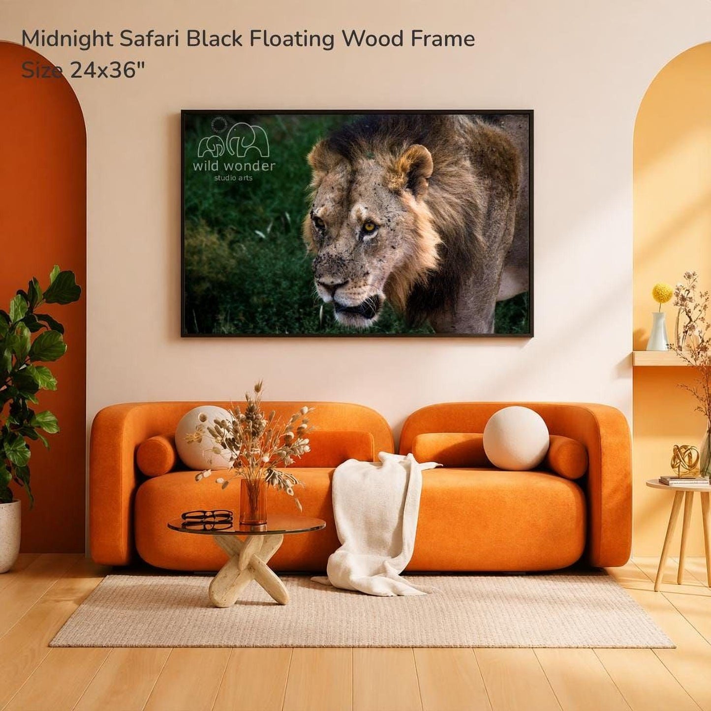 a large, framed photograph of a lion on the wall of a living room. The lion is depicted in a black floating wood frame, which is mounted above a couch and a coffee table. The couch is an orange sofa, and the coffee table has a glass top. The room has a warm, inviting atmosphere with a rug on the floor and some decorative elements like a vase and a potted plant.