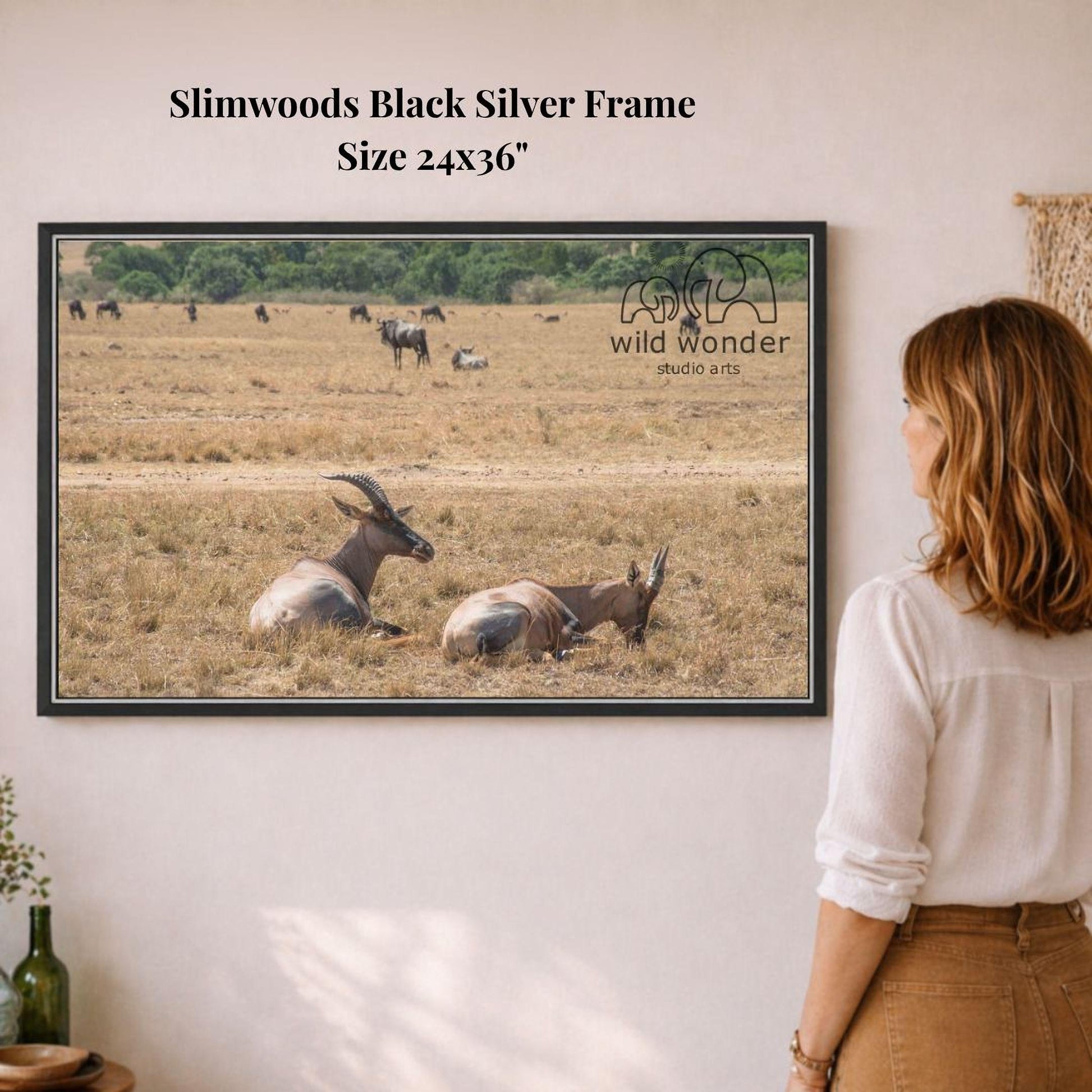 A woman is standing in front of a framed photograph of a group of animals, including antelopes and gazelles, in a field.