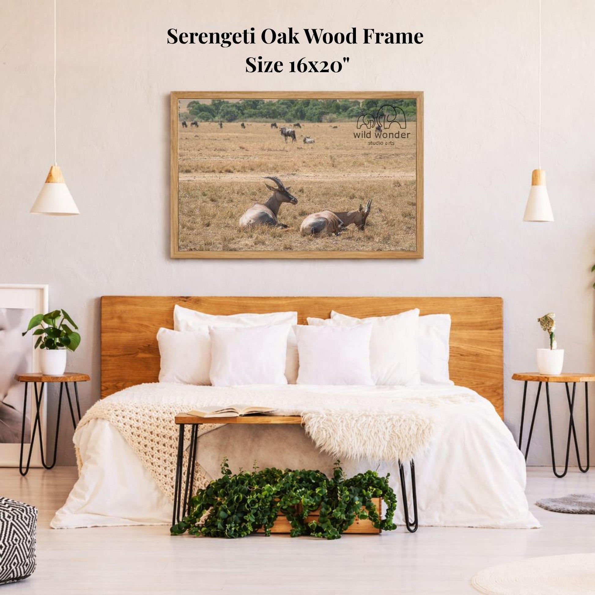 a serene bedroom scene with a large framed picture of a herd of antelopes resting in a field above a bed with white bedding.