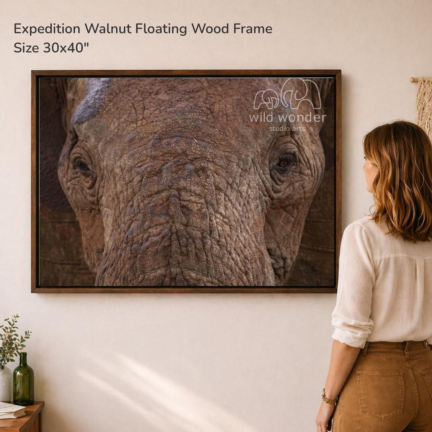 A woman is standing in front of a large framed photograph of an elephant, looking at the artwork on the wall.