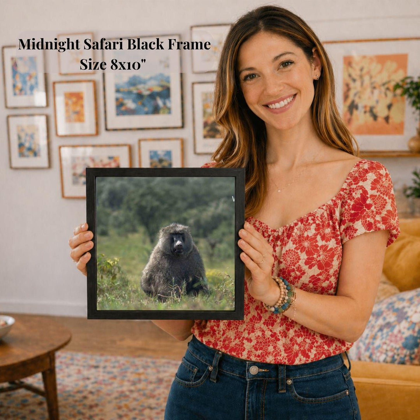 A woman is holding a framed picture of a monkey in a grassy field, with a smiling expression on her face.