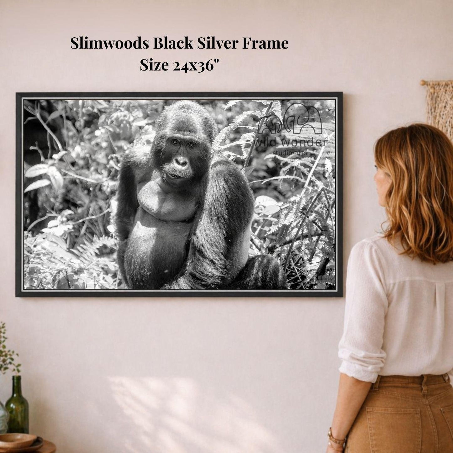 A woman is standing in front of a framed black and white photograph of a gorilla, which is hanging on a wall.