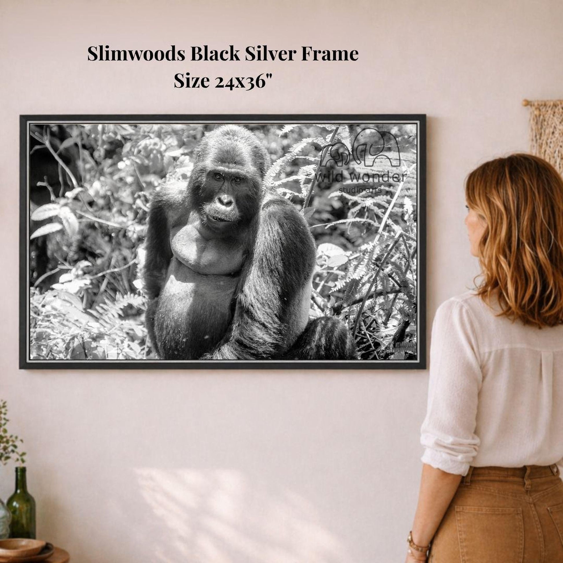 A woman is standing in front of a framed black and white photograph of a gorilla, which is hanging on a wall.
