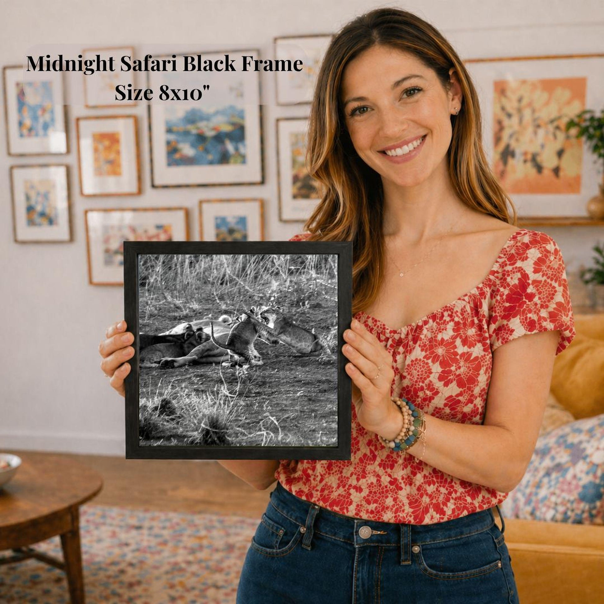 A woman is holding a framed black and white photograph of a lion in a grassy field, with a smiling expression.