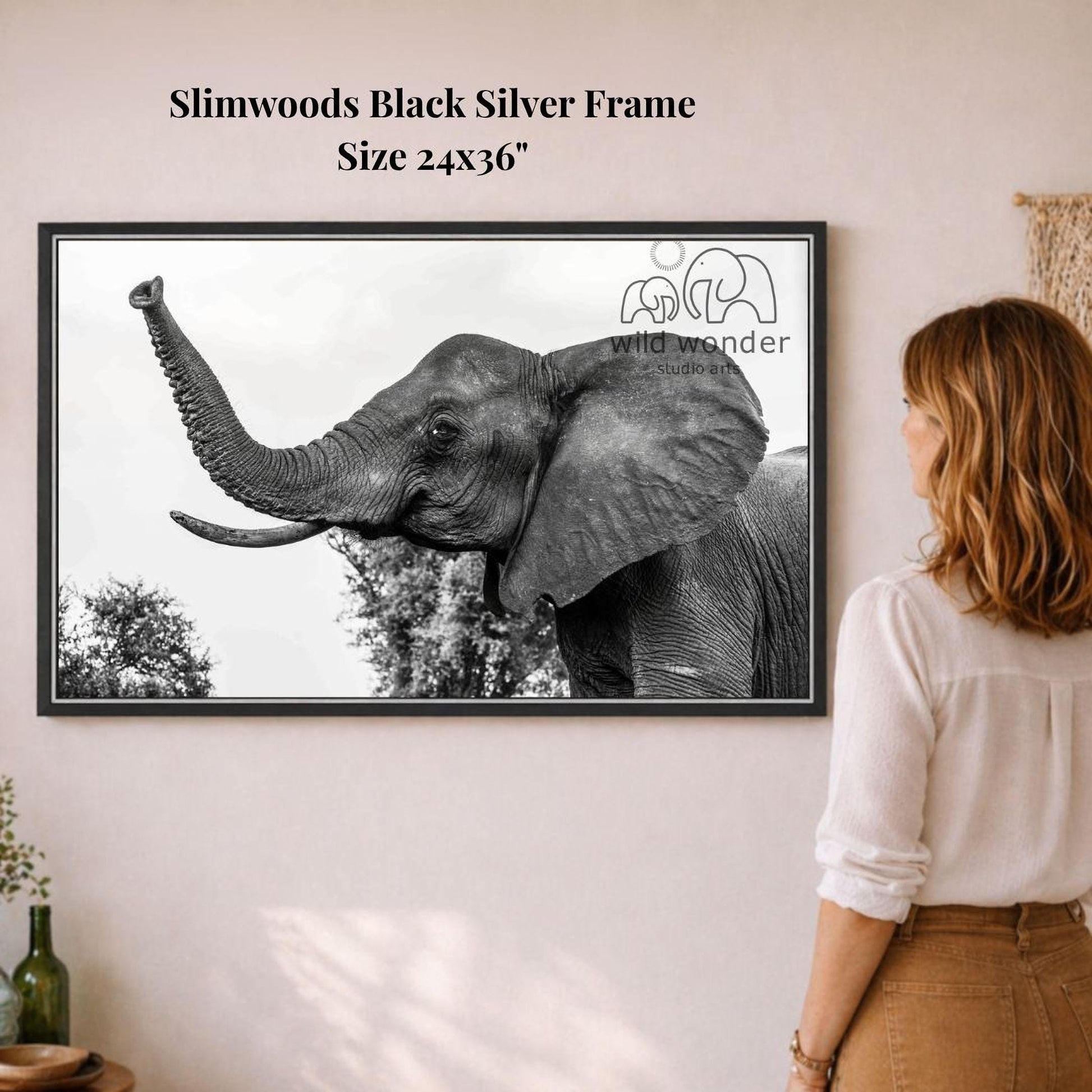 A woman is standing in front of a framed photograph of an elephant, looking at it with interest.