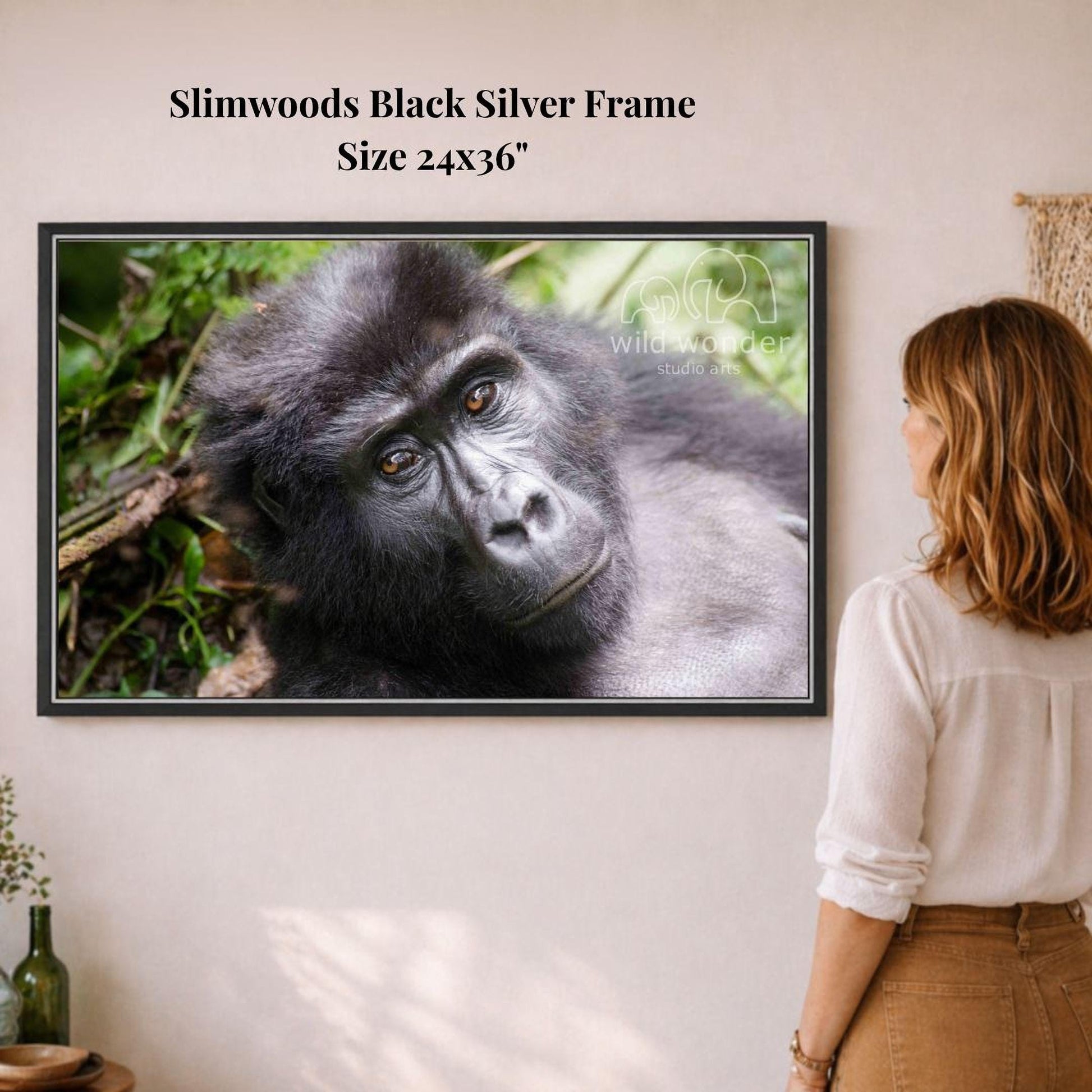 A woman is standing in front of a framed photograph of a gorilla, looking at the artwork on the wall.