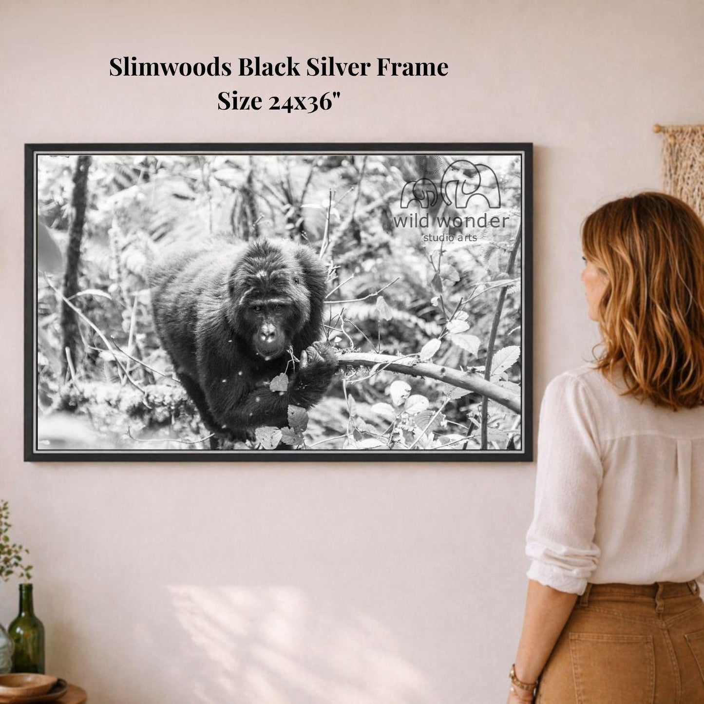 A woman is standing in front of a framed black and white photograph of a gorilla in a forest, looking at the artwork.