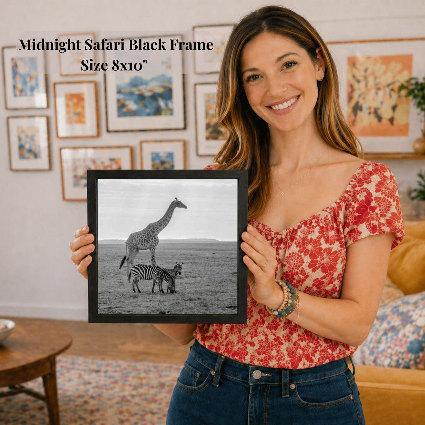 A woman is holding a framed photograph of a giraffe and a zebra in a savannah landscape, with a black and white image of the animals.