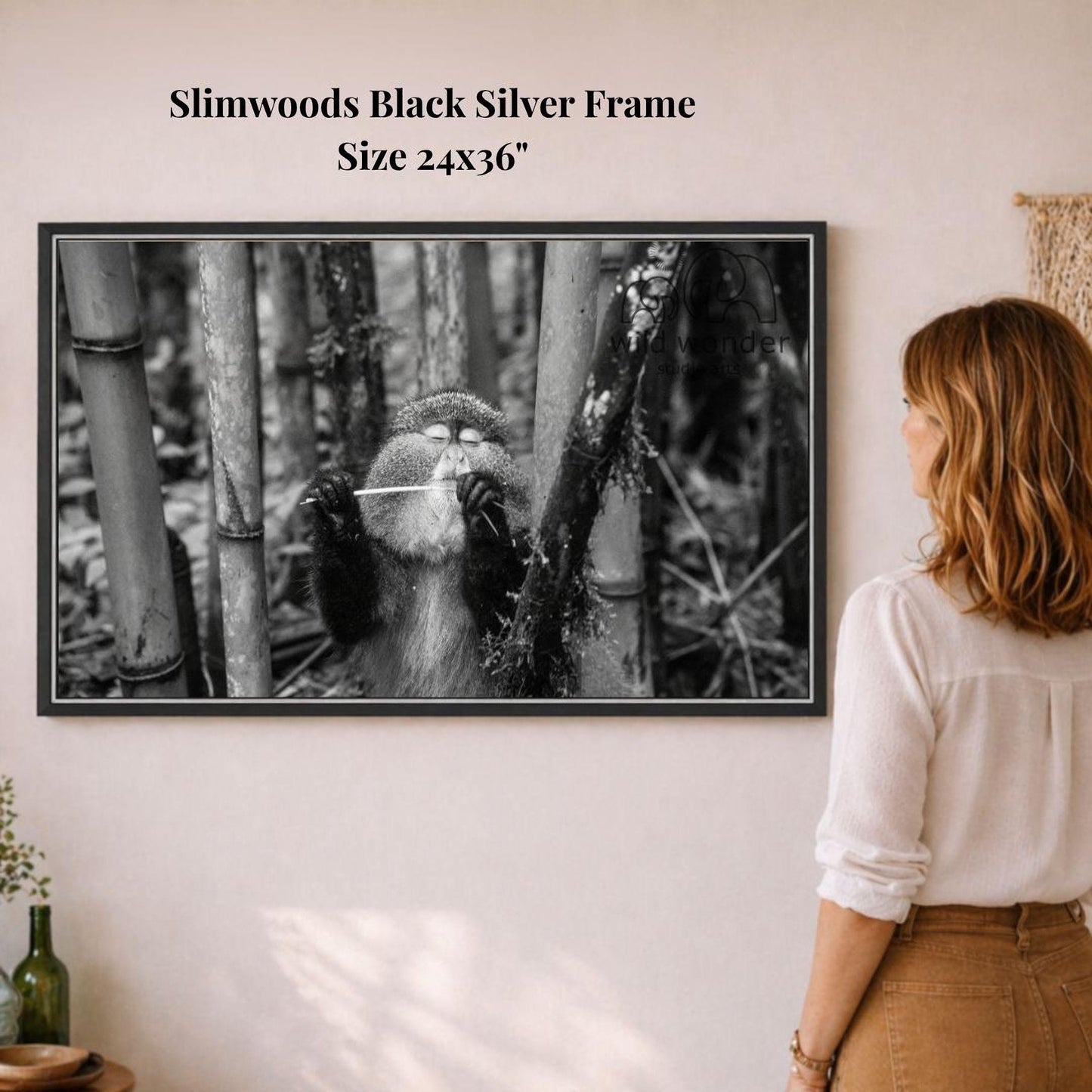 A woman is standing in front of a framed black and white photograph of a monkey playing a string instrument, surrounded by bamboo trees.