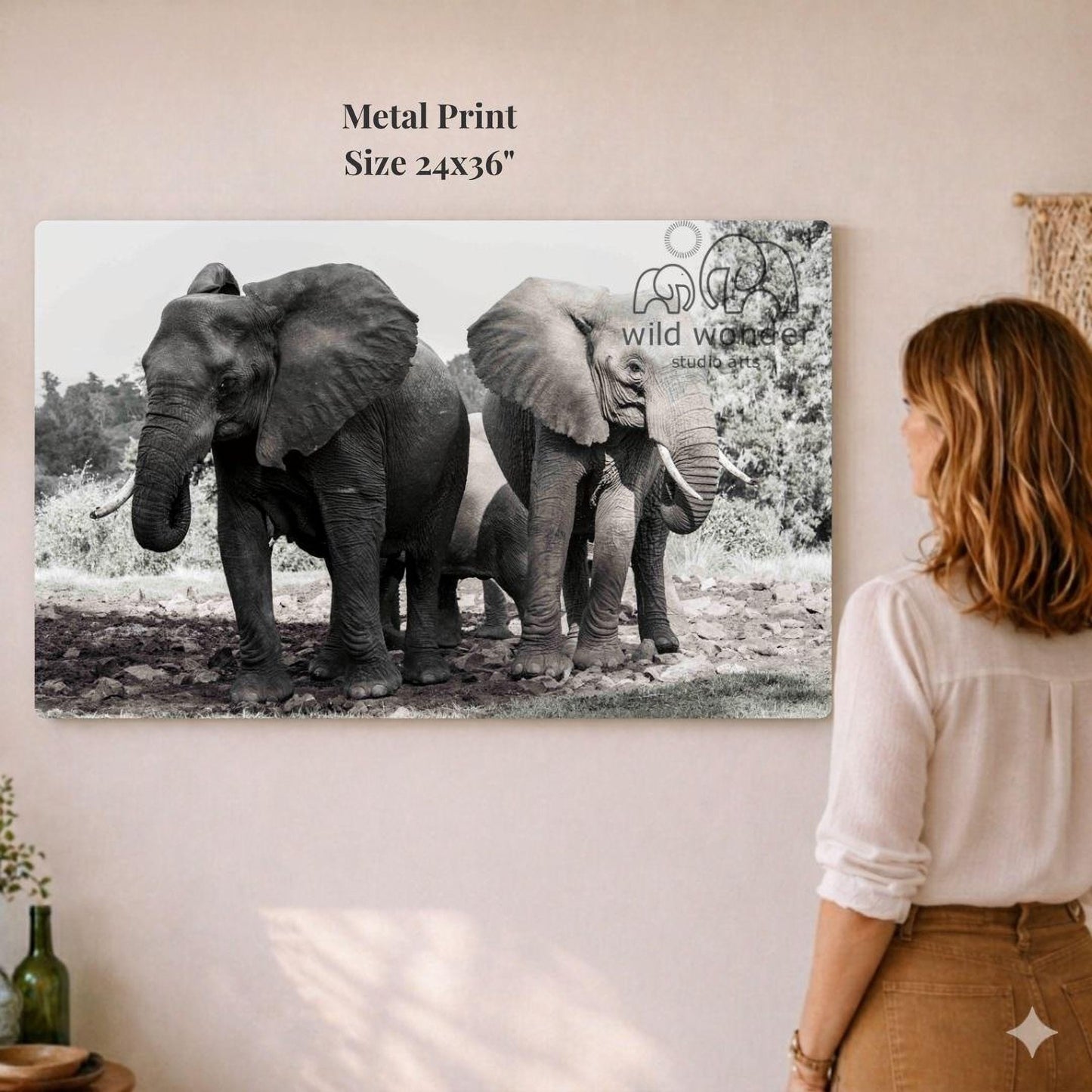 A woman is standing in front of a large metal print depicting a group of elephants in a natural setting.