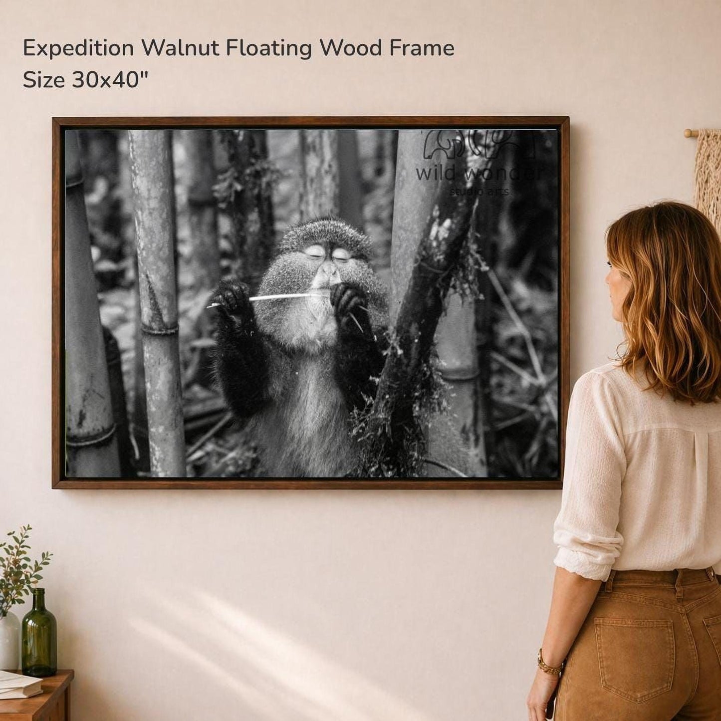 A woman is standing in front of a large framed photograph of a monkey in a forest setting, looking at the artwork.