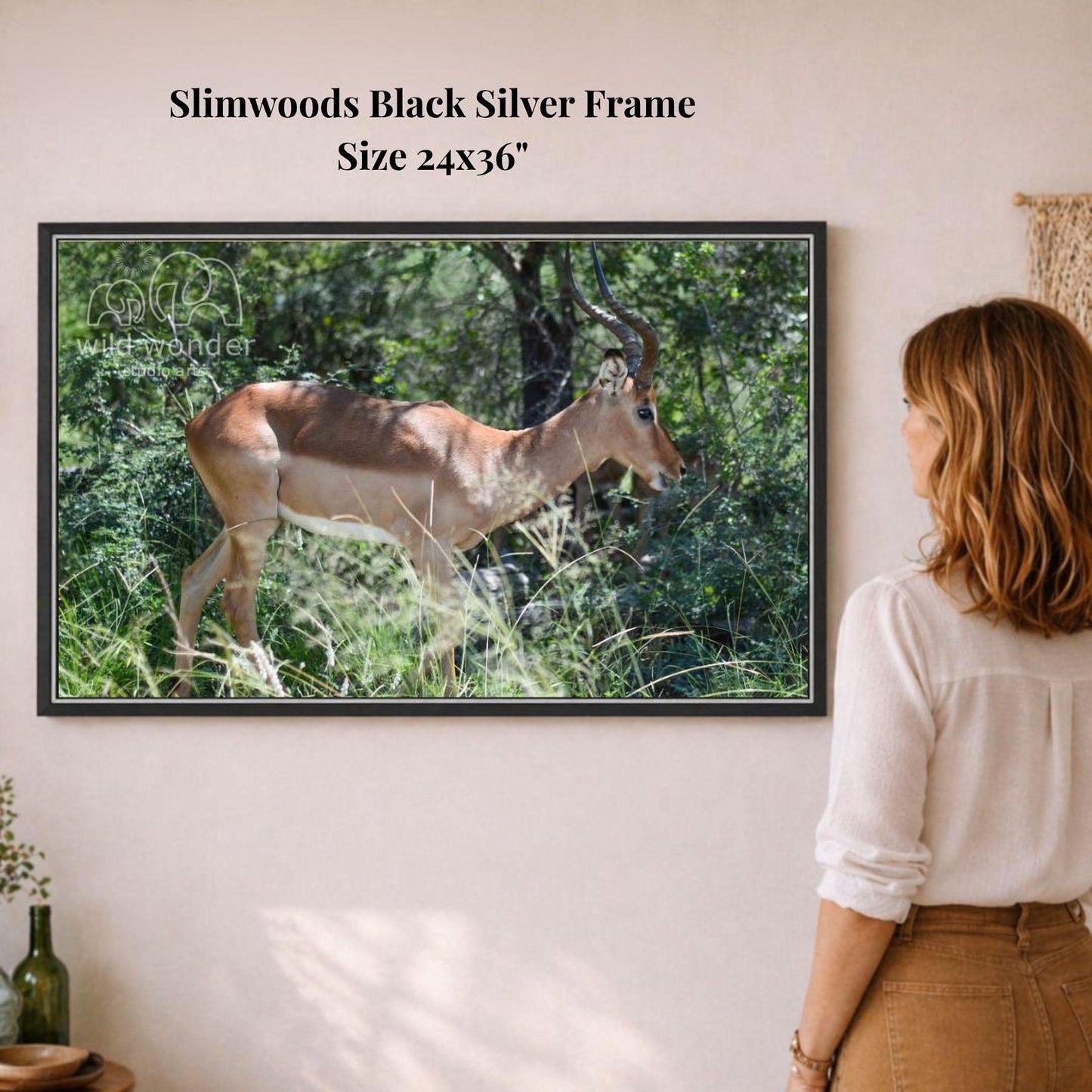 A woman is standing in front of a framed photograph of a gazelle in a grassy field, observing the animal.