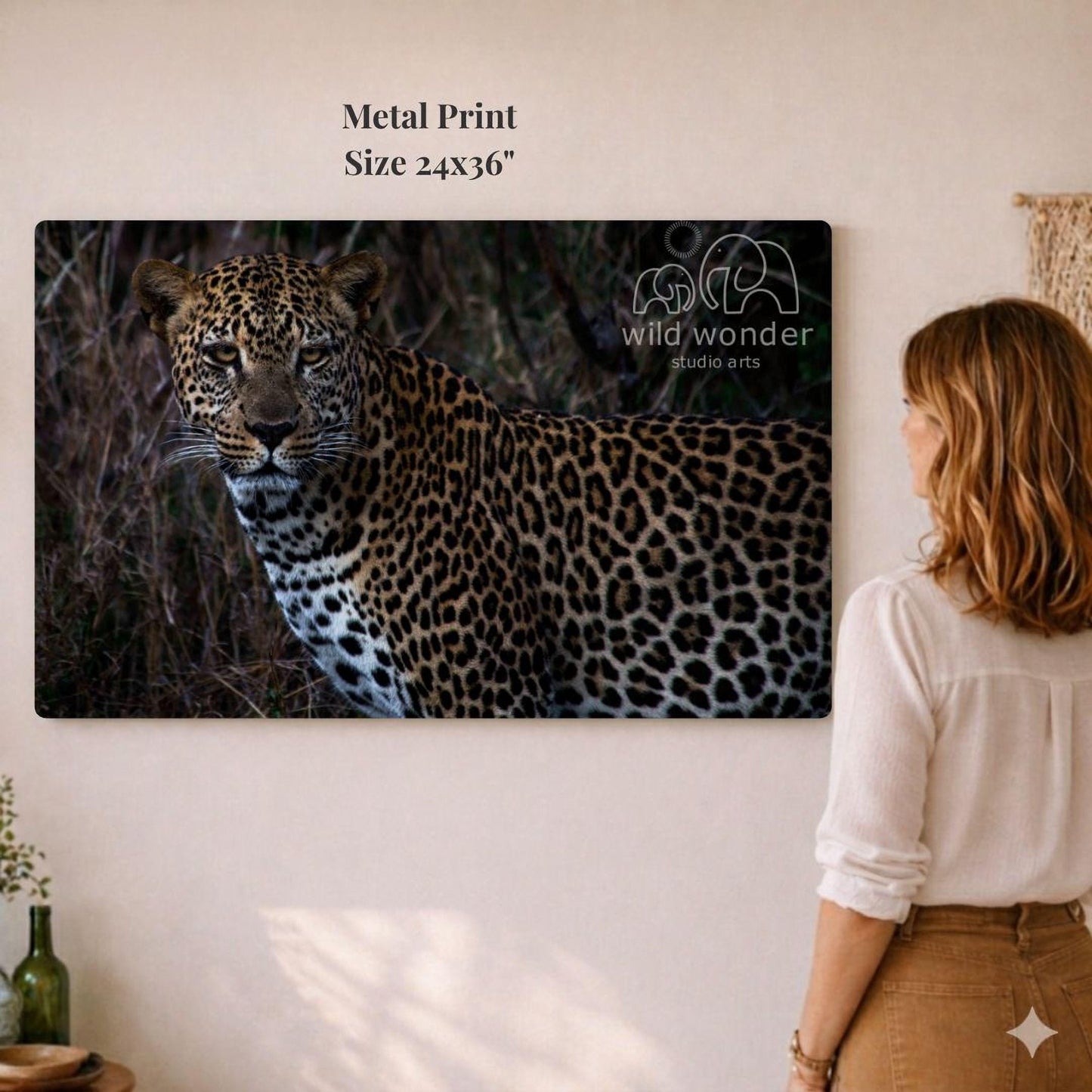 A woman is standing in front of a large metal print depicting a leopard in its natural habitat.