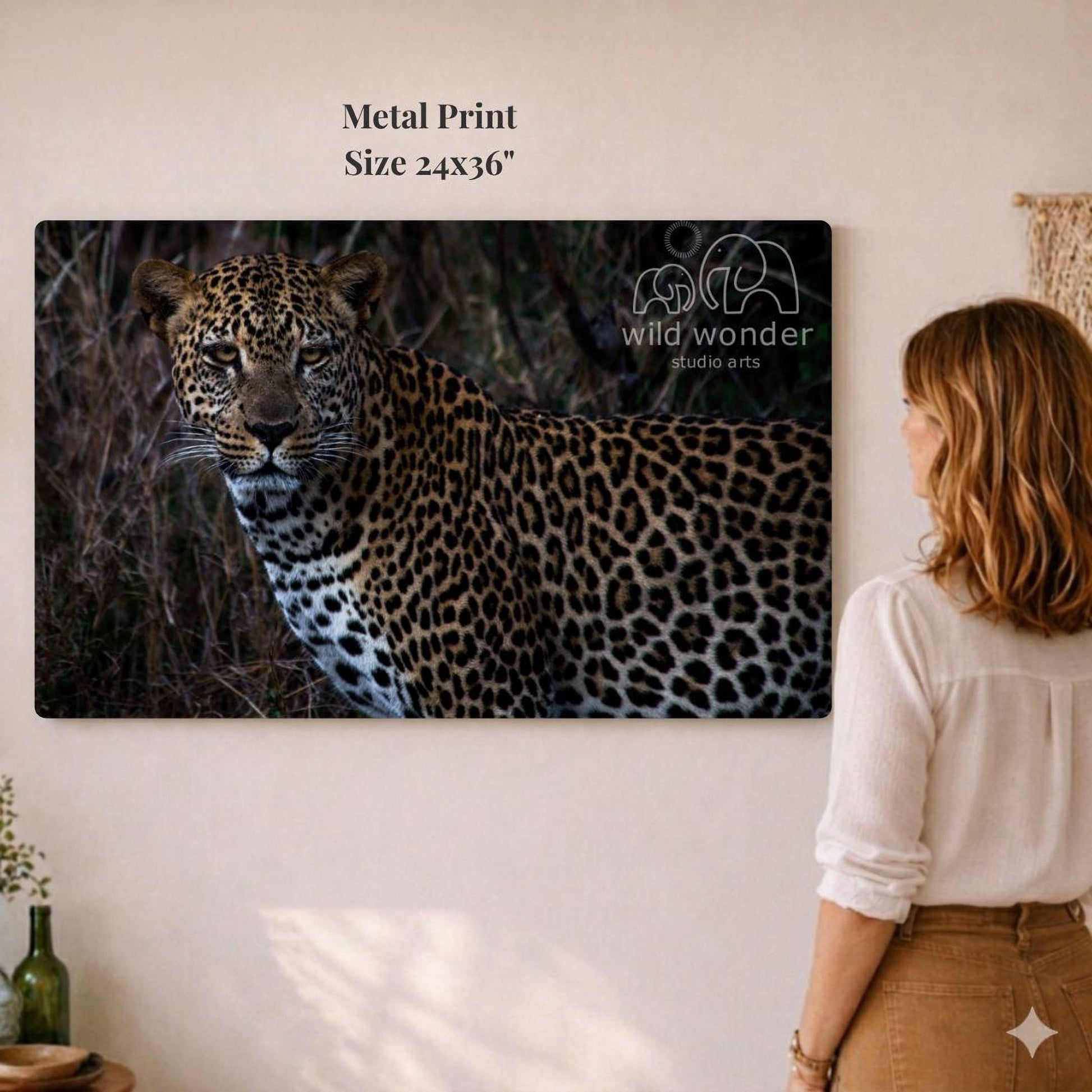 A woman is standing in front of a large metal print depicting a leopard in its natural habitat.