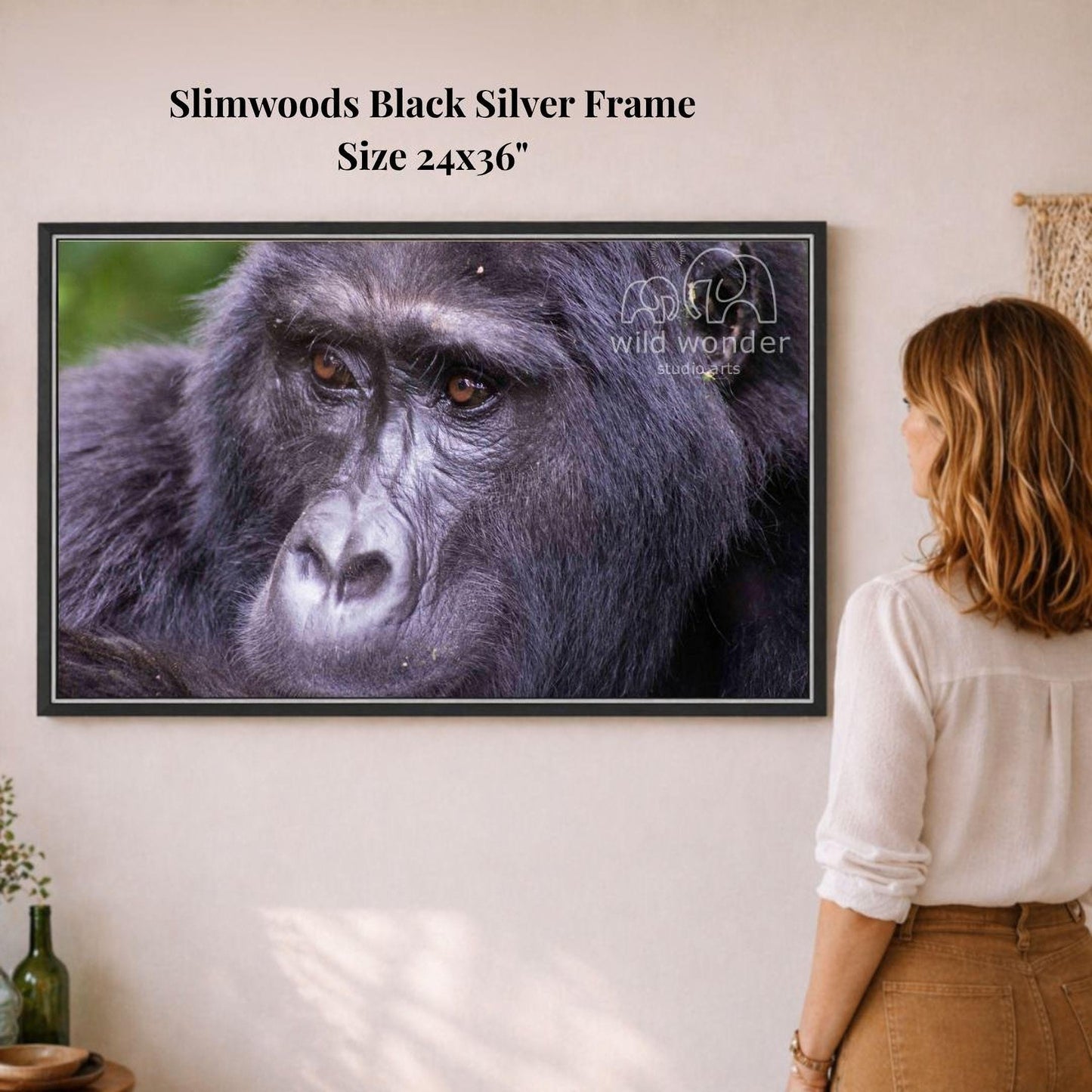 A woman is standing in front of a framed photograph of a gorilla, looking at it with interest.