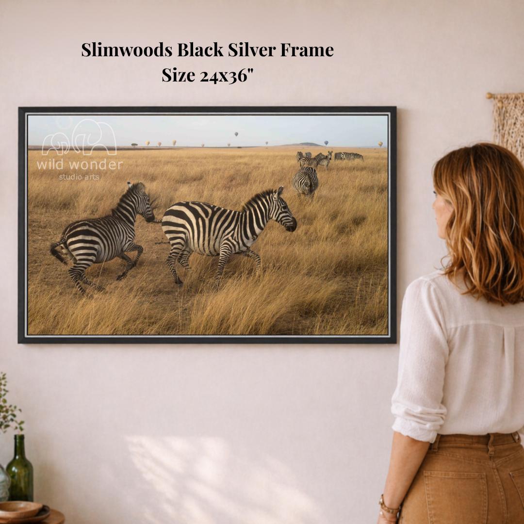 A woman is standing in front of a framed photograph of two zebras in a grassy field, looking at the artwork.