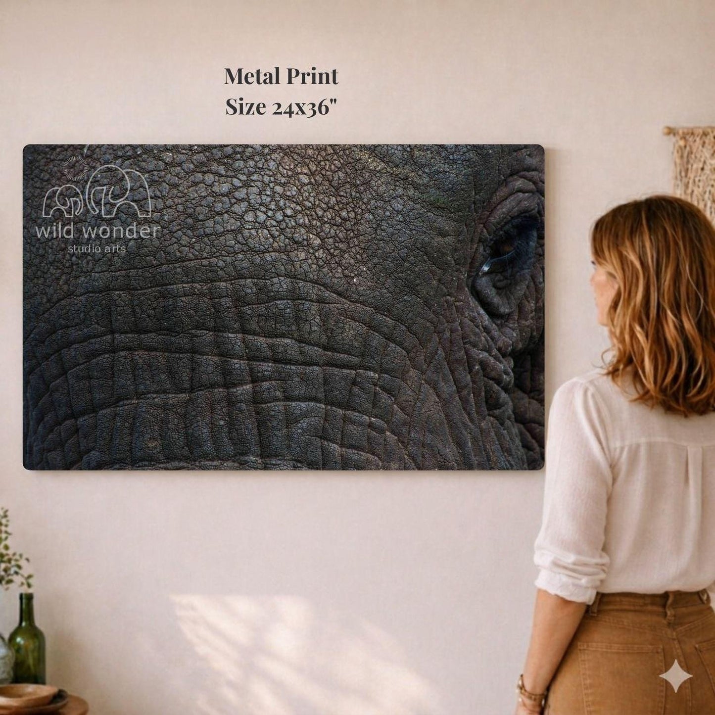 A woman is standing in front of a large metal print of an elephant's eye, looking at it with interest.
